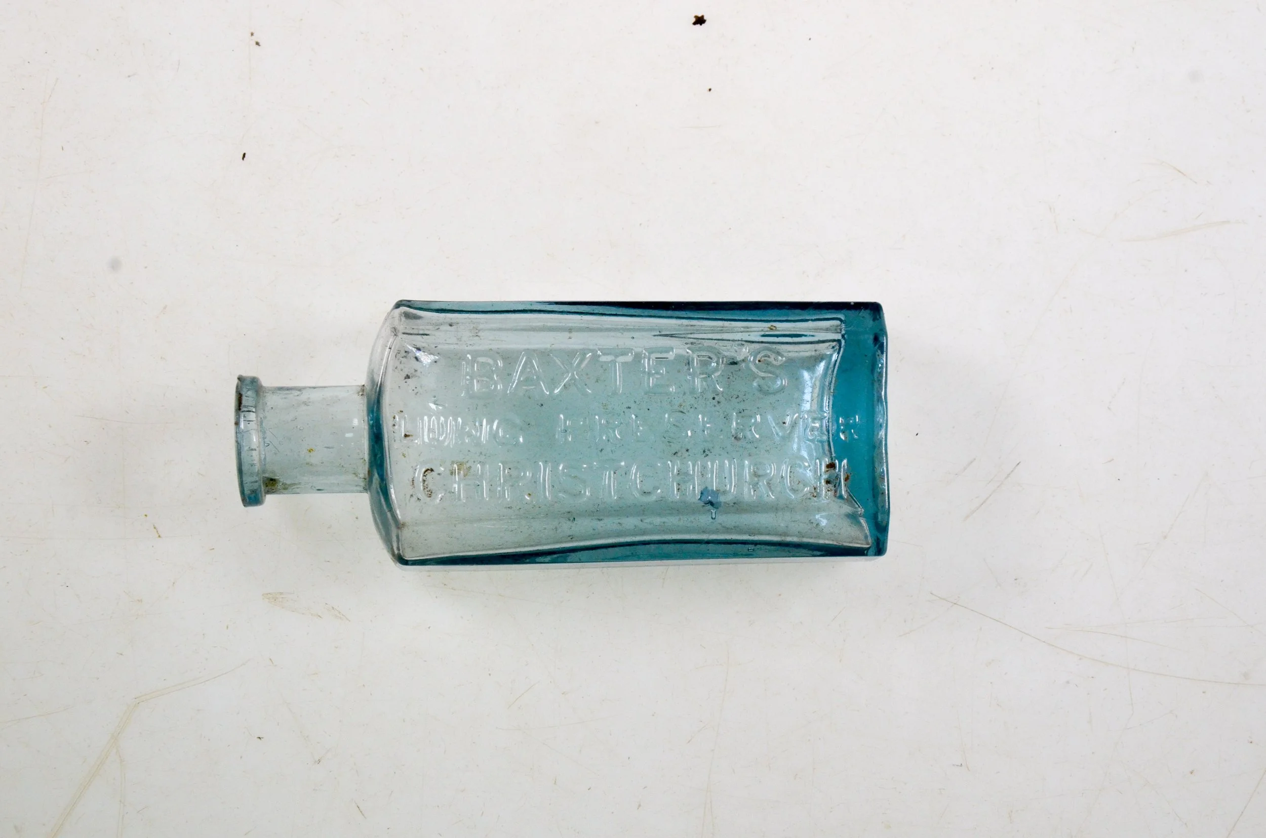 Old glass bottle with embossed text reading 'BAXTER'S LONDON & KENT CHURCH' on a white surface.