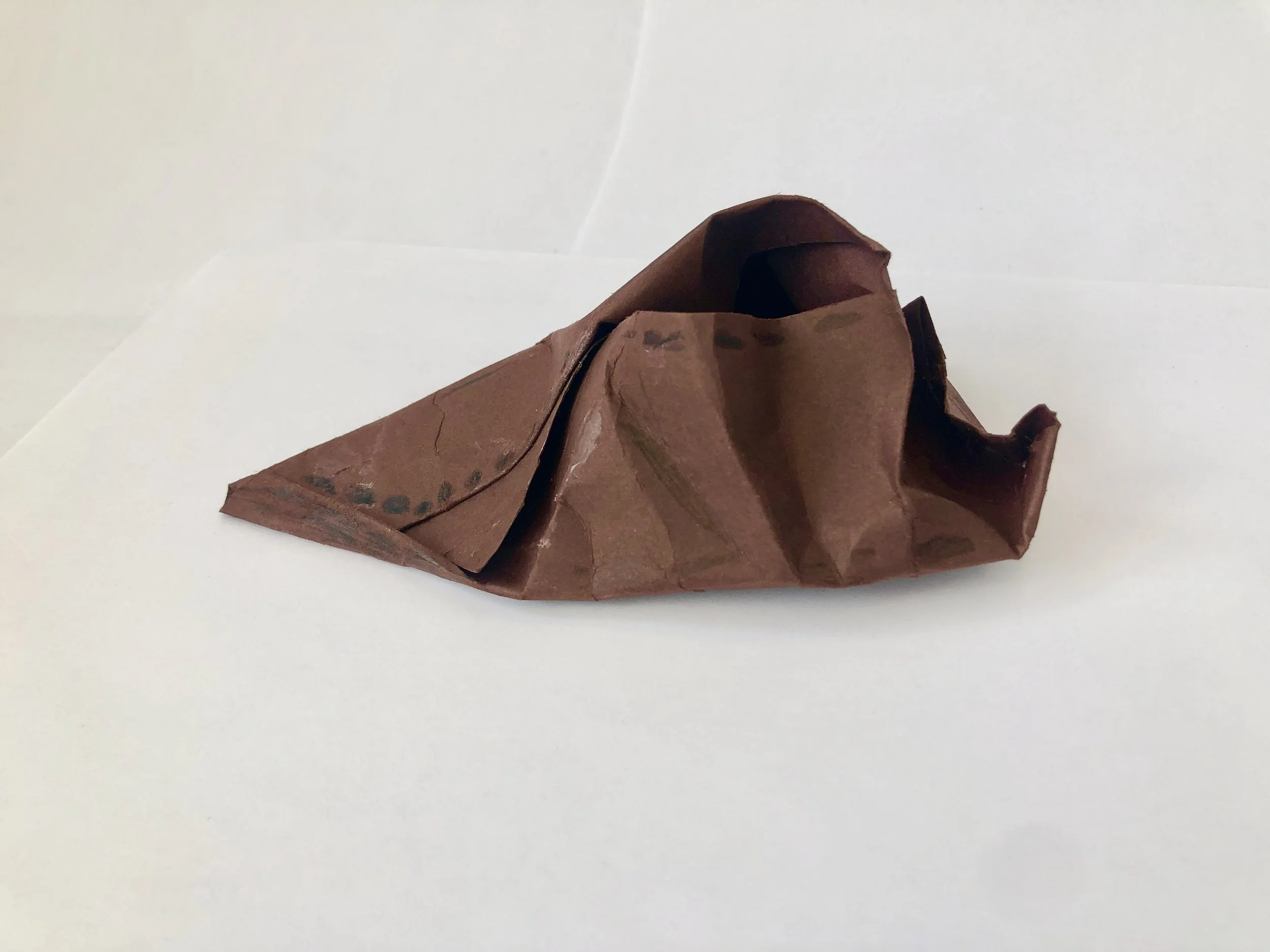 Crinkled brown paper in the shape of a mountain on a white surface.