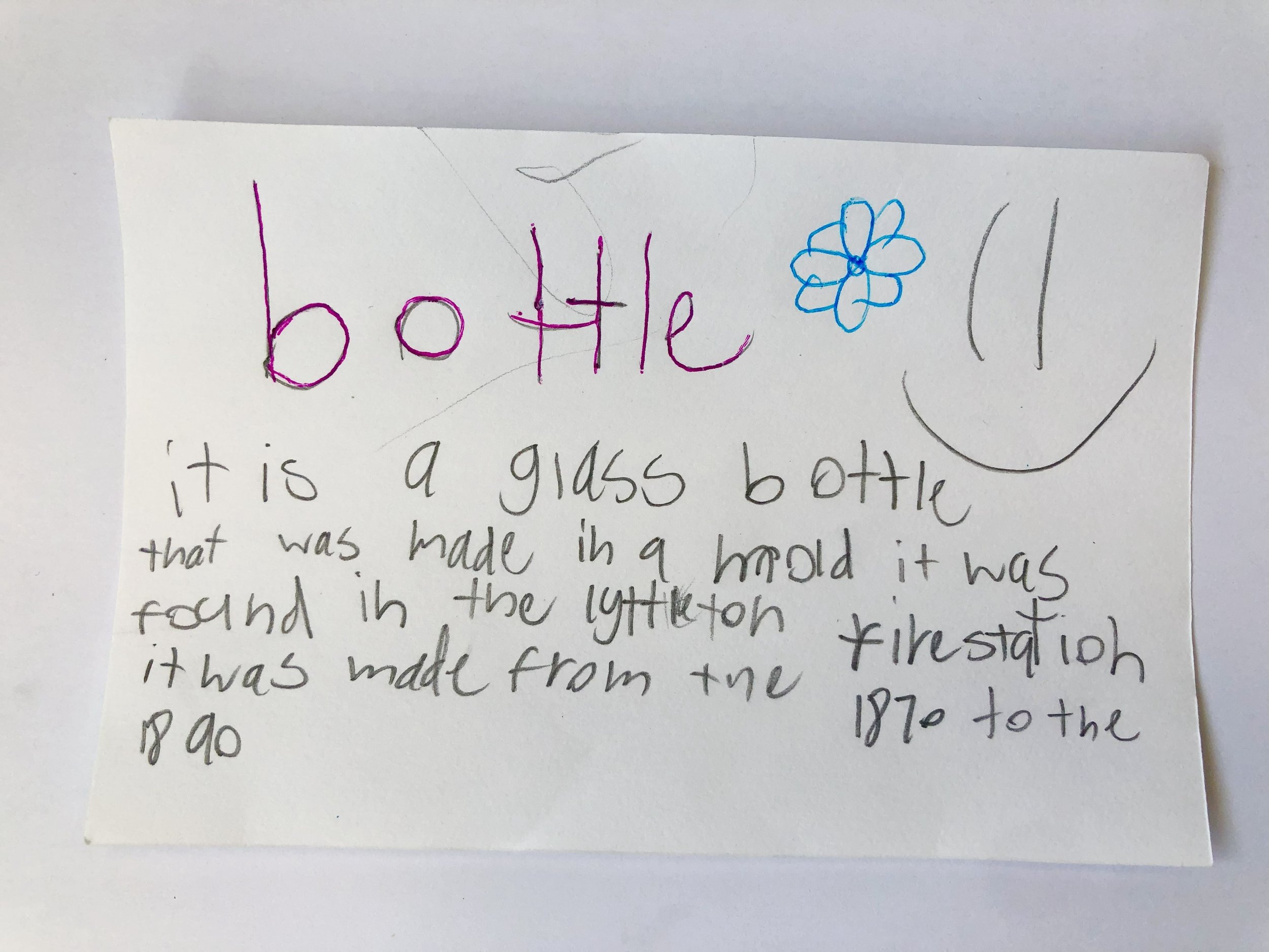 Handwritten note about a glass bottle with a blue flower drawing, describing its history and origin, with a smiley face drawn on the right.