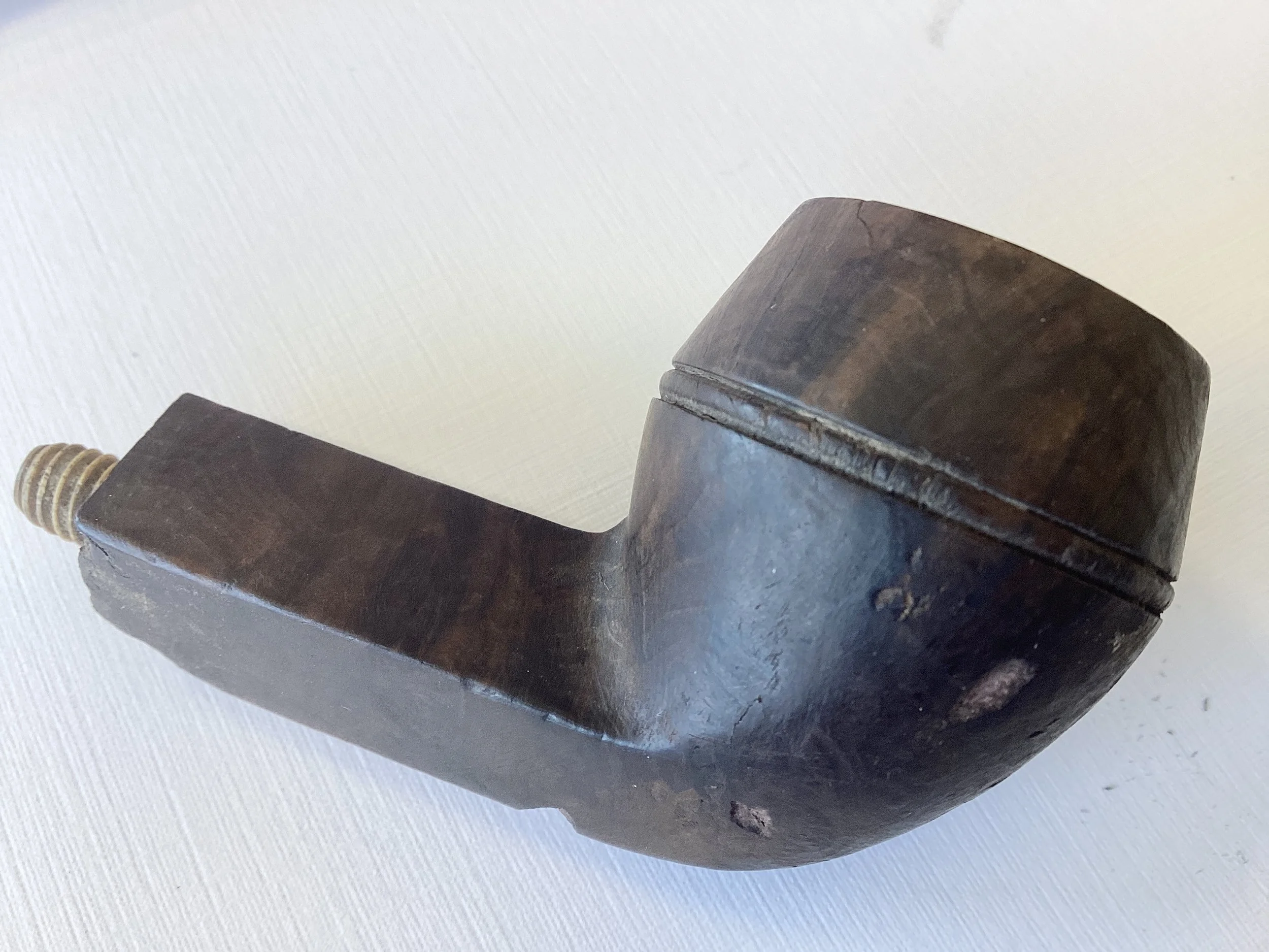 A dark wooden object with a brass screw at one end, resembling a vintage or antique tool or device, resting on a white textured surface.