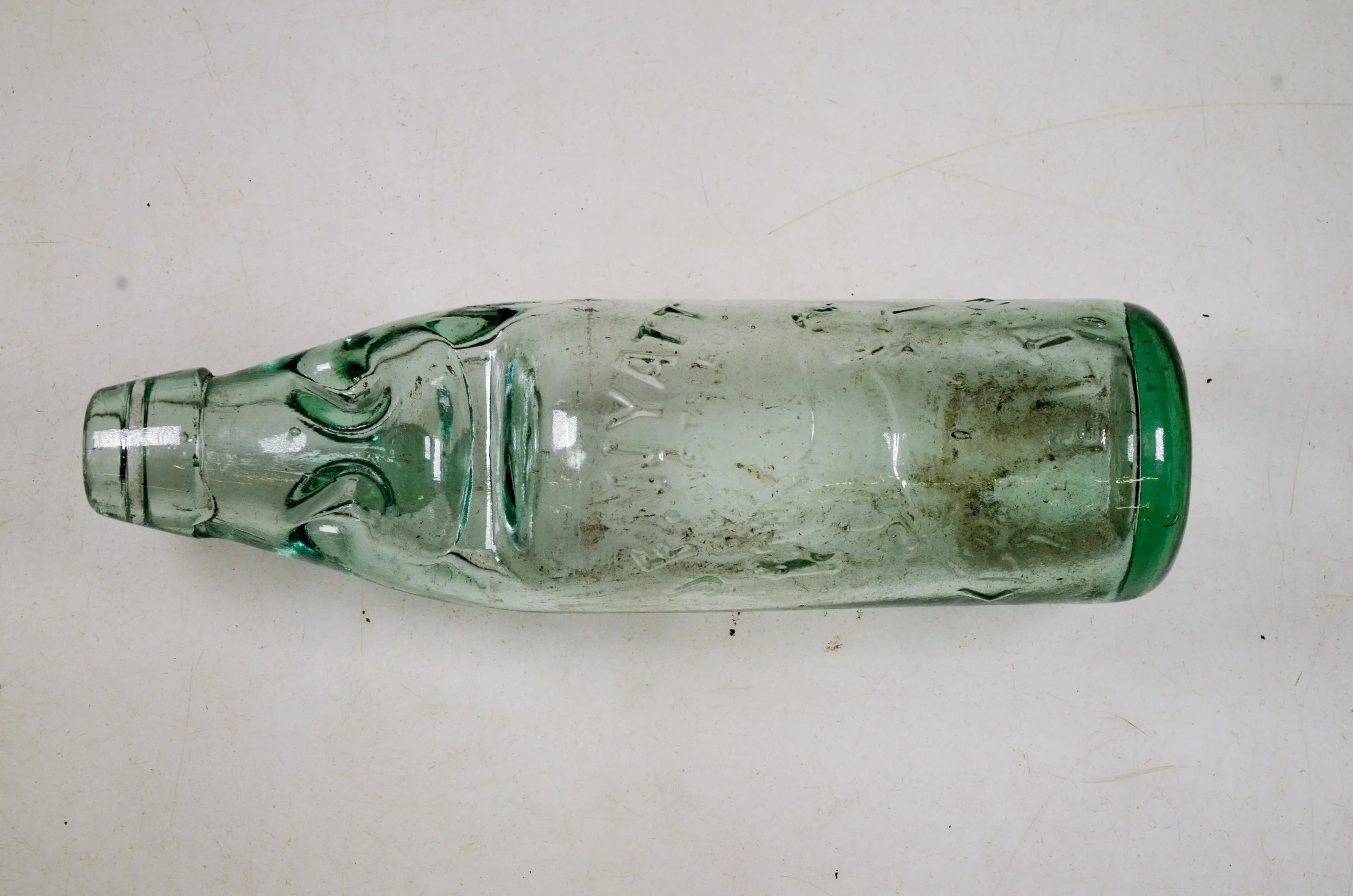 A glass bottle with a carved face design, resembling an Easter Island Moai statue, lying horizontally on a white surface.