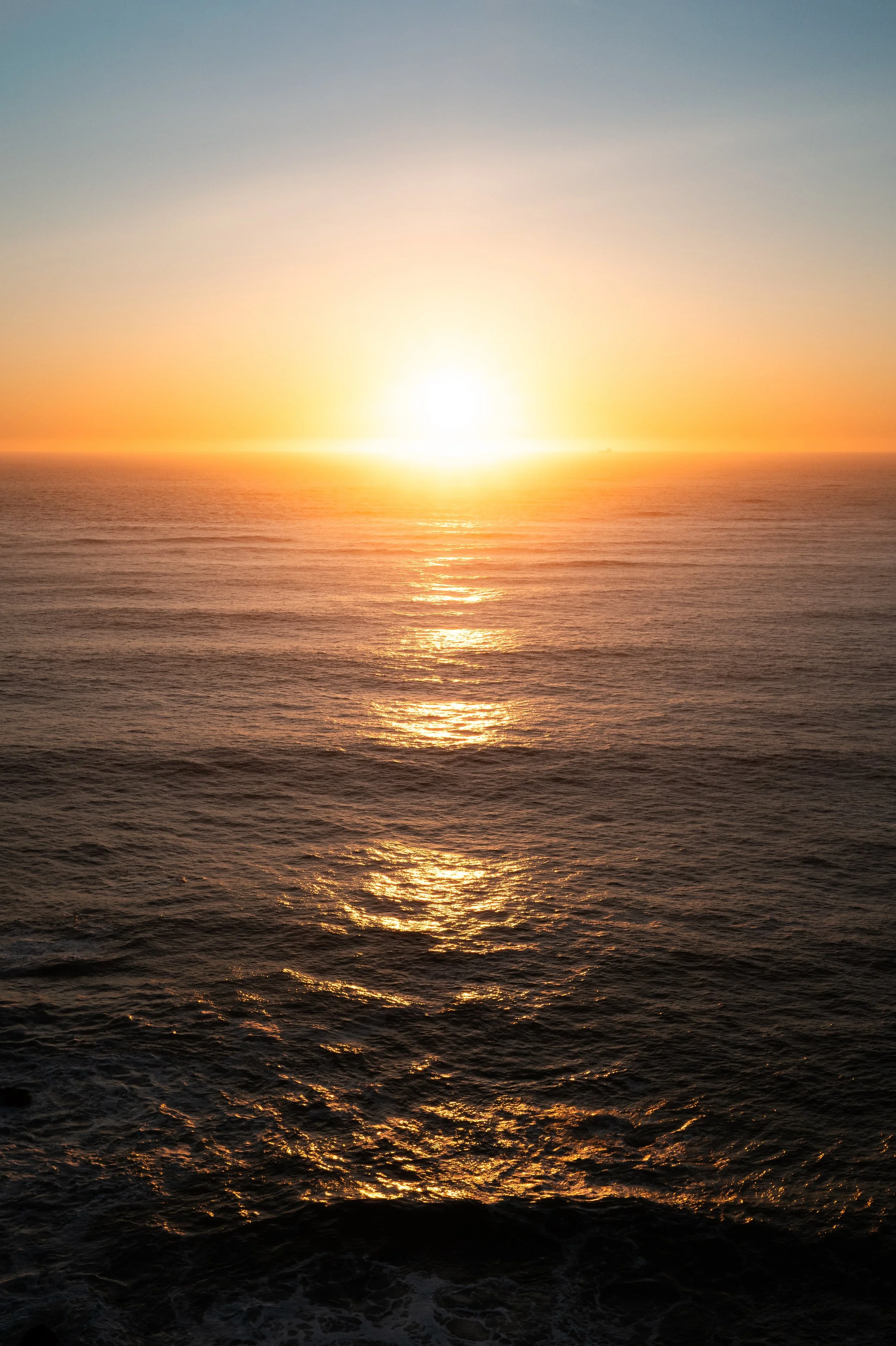 Sunset over the ocean with the sun near the horizon, reflecting off the water.