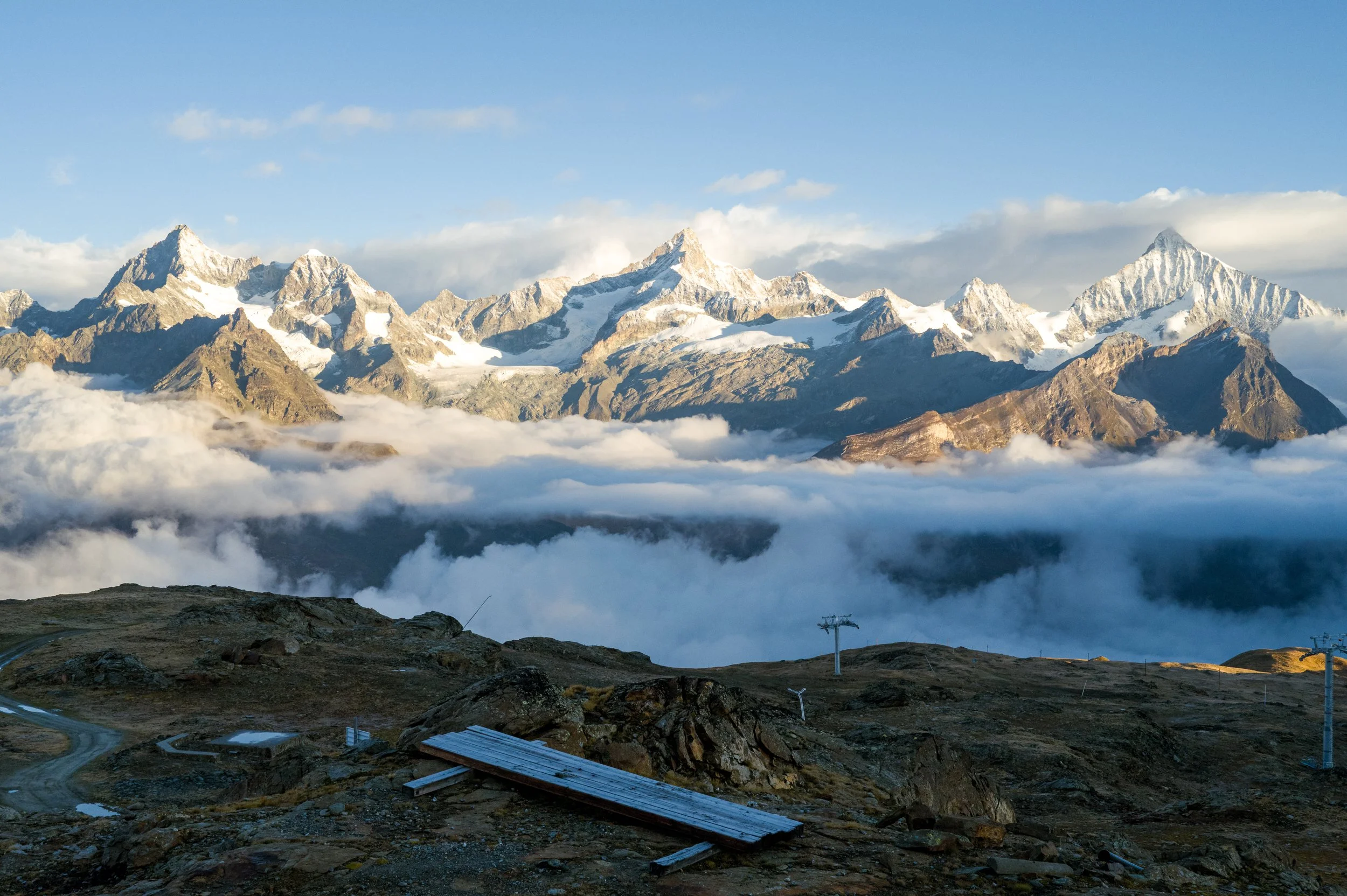 Snow-capped mountain range with cloud cover and a rocky foreground with ski lift structures in the Swiss Alps.
