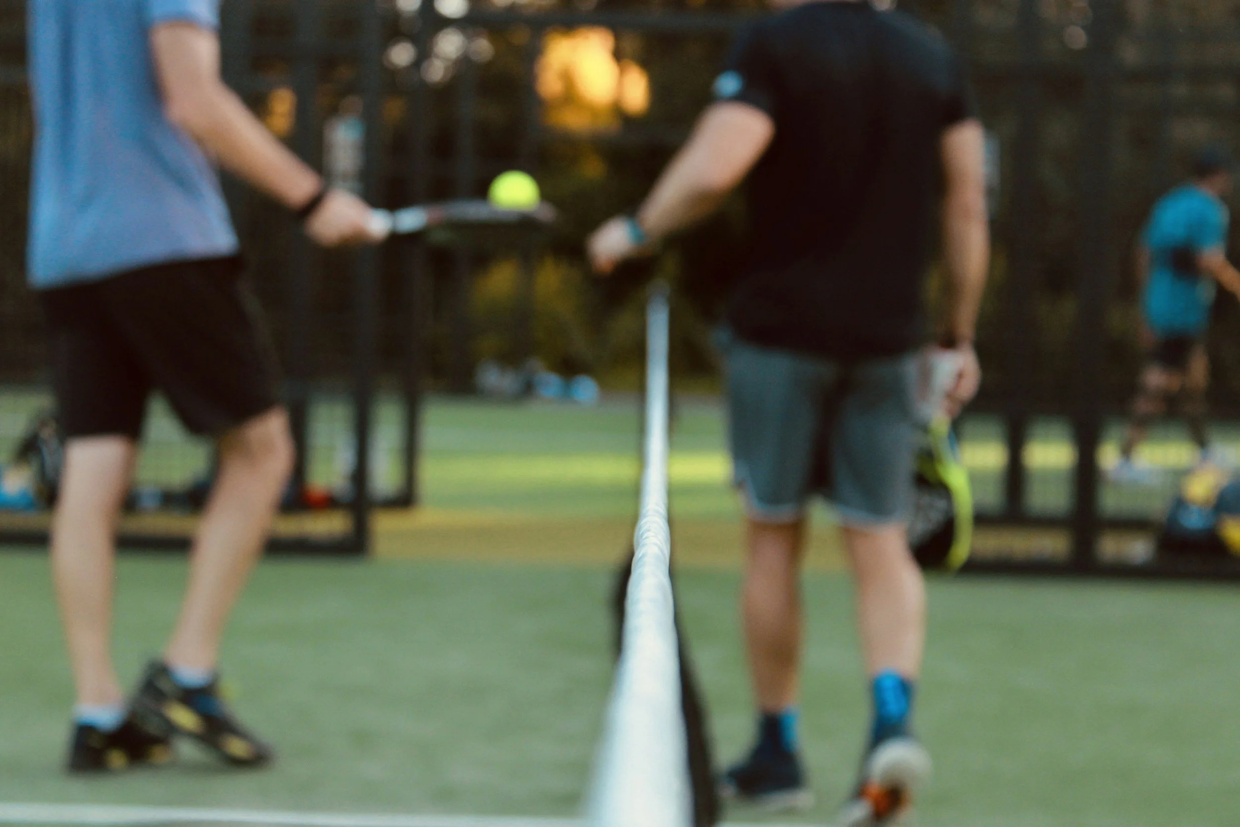 People playing pickleball on an outdoor court in the evening.