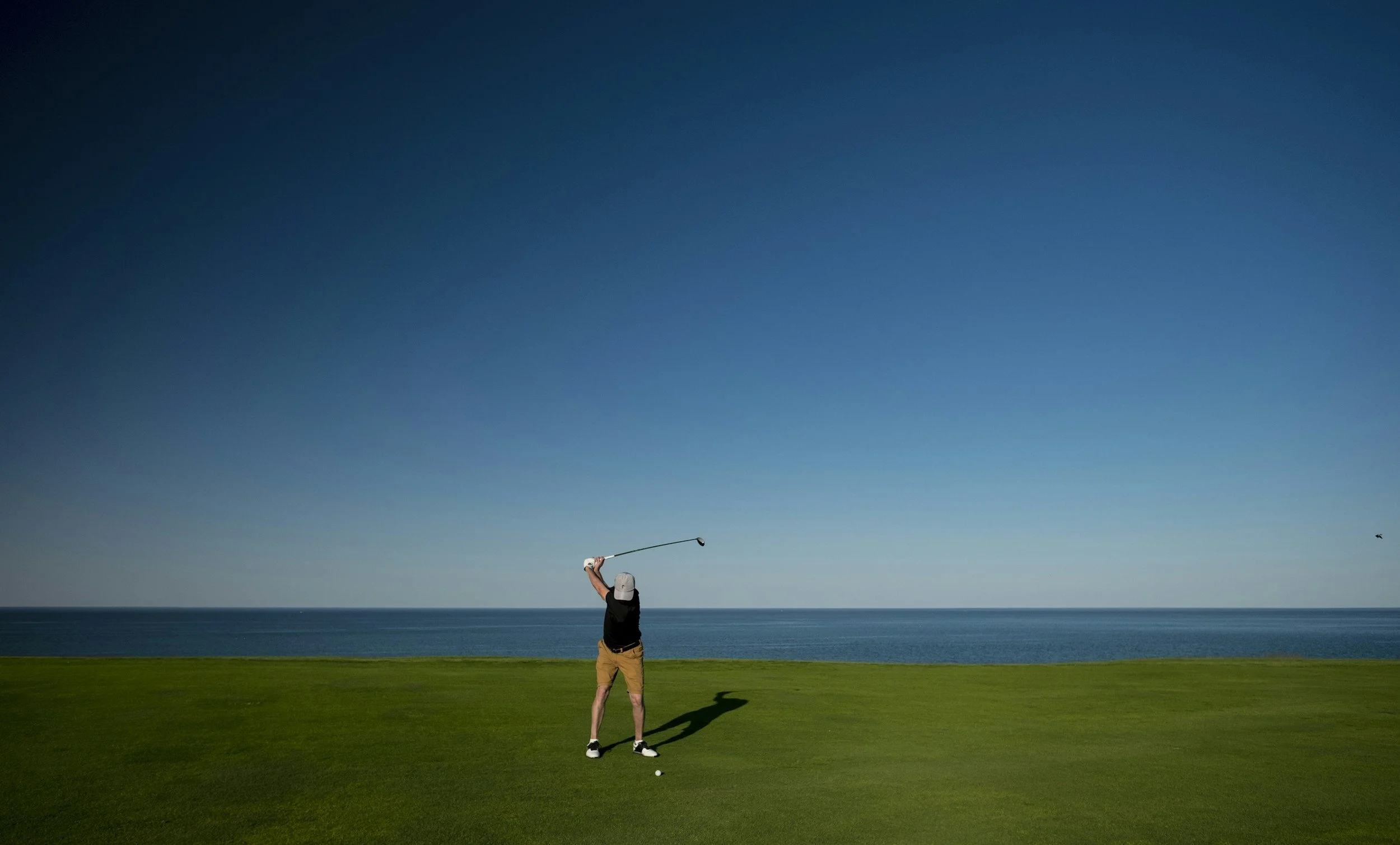 A person playing golf on a course near the coast under a clear blue sky.