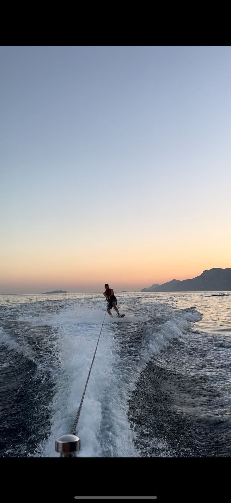 A person wakeboarding on the water during sunset with mountains in the background.