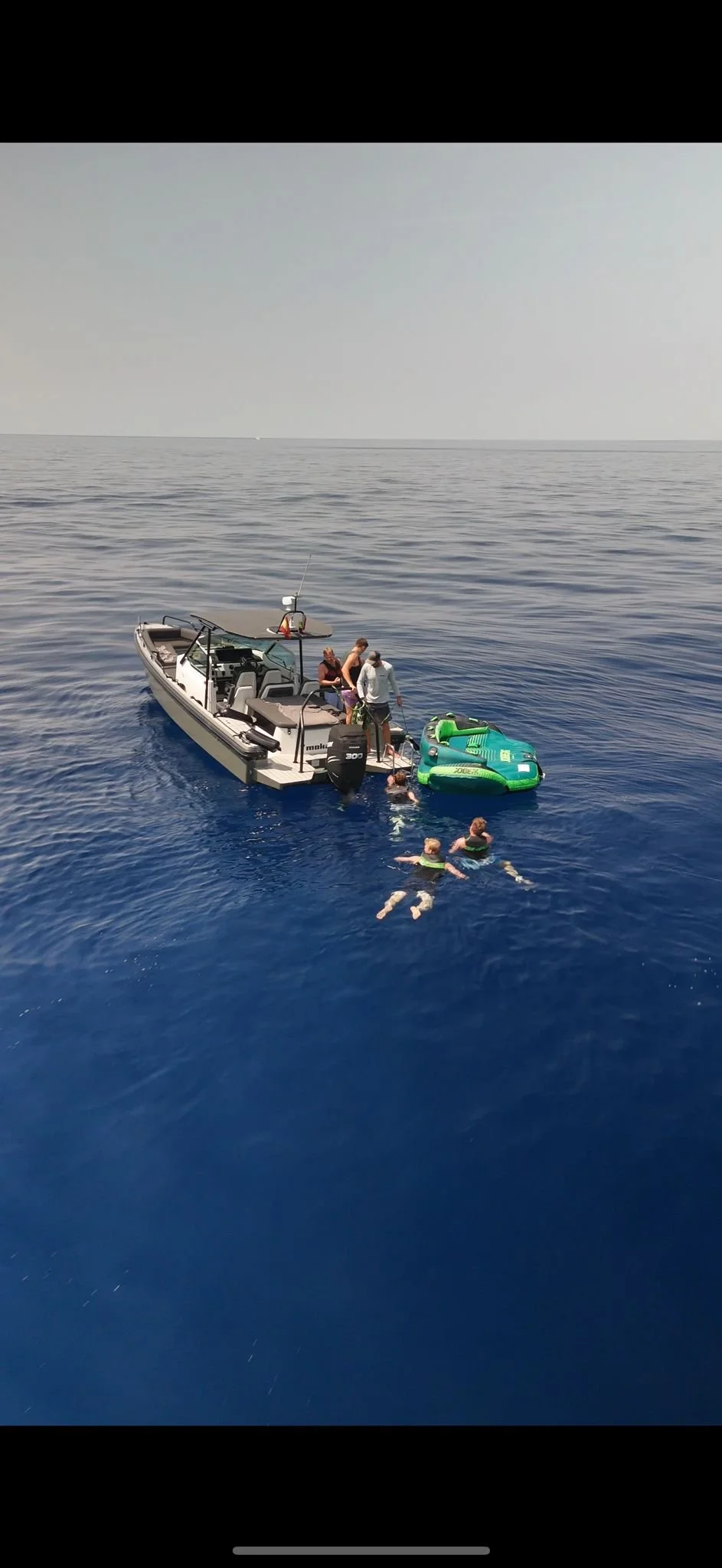 Group of people swimming and standing in the ocean near a boat with another inflatable boat nearby.