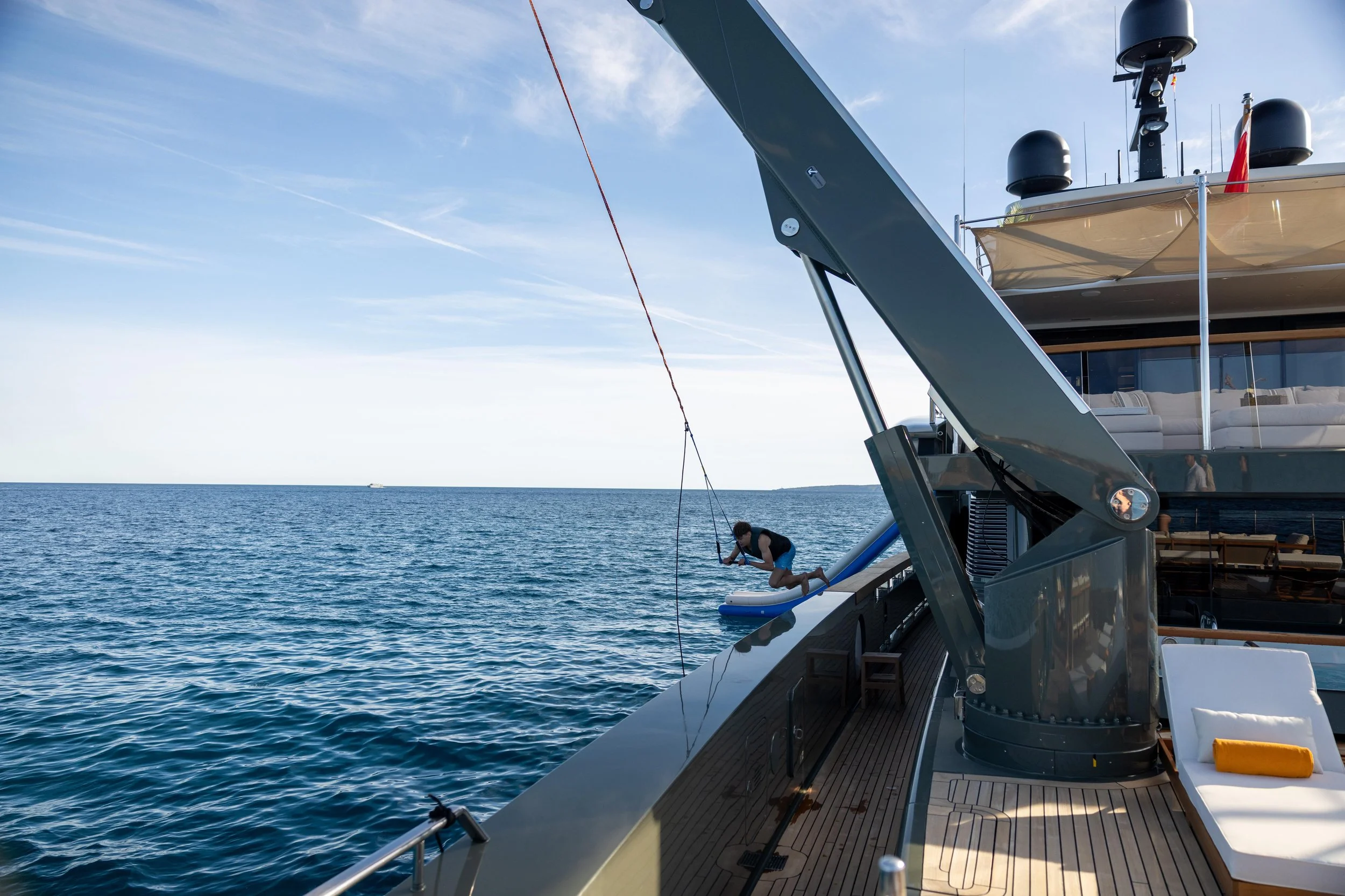 Child jumping off the side of a yacht into the water, with a view of the open ocean and clear sky in the background.