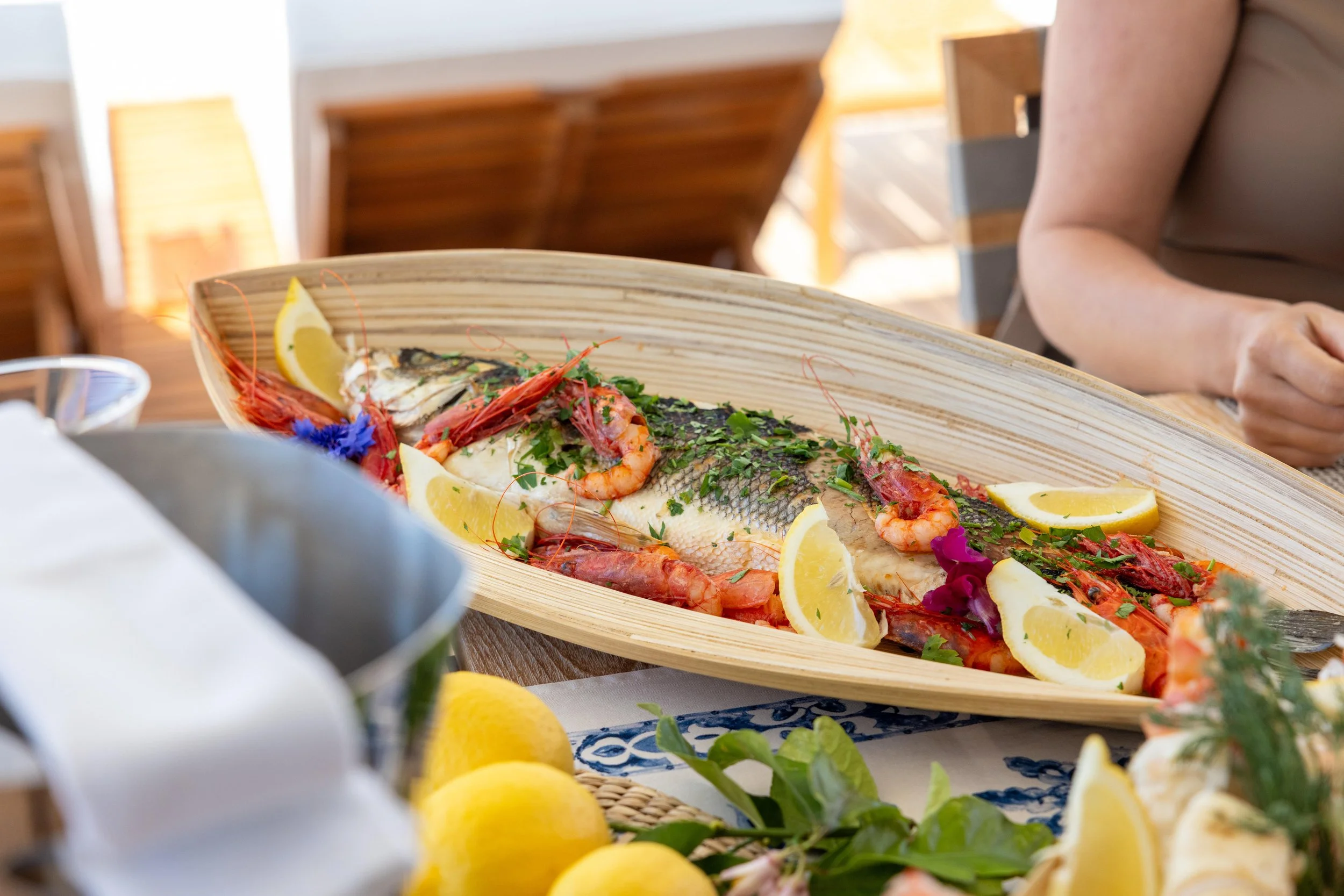Seafood platter featuring fish, shrimp, lemon wedges, and herbs served on a wooden boat-shaped tray.