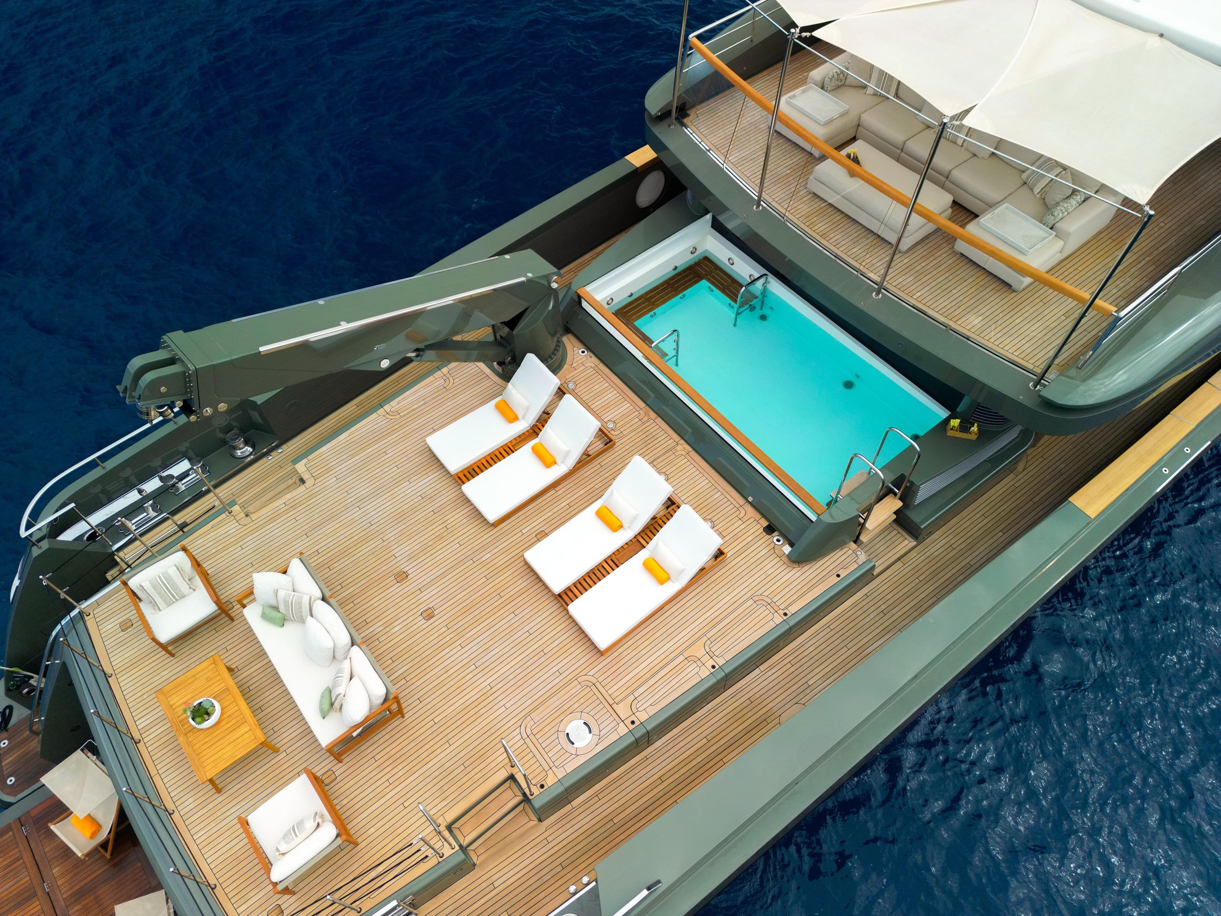 Aerial view of a luxury yacht deck at sea with a swimming pool, sun loungers, outdoor seating, and a shaded lounge area. Motor yacht Moka.