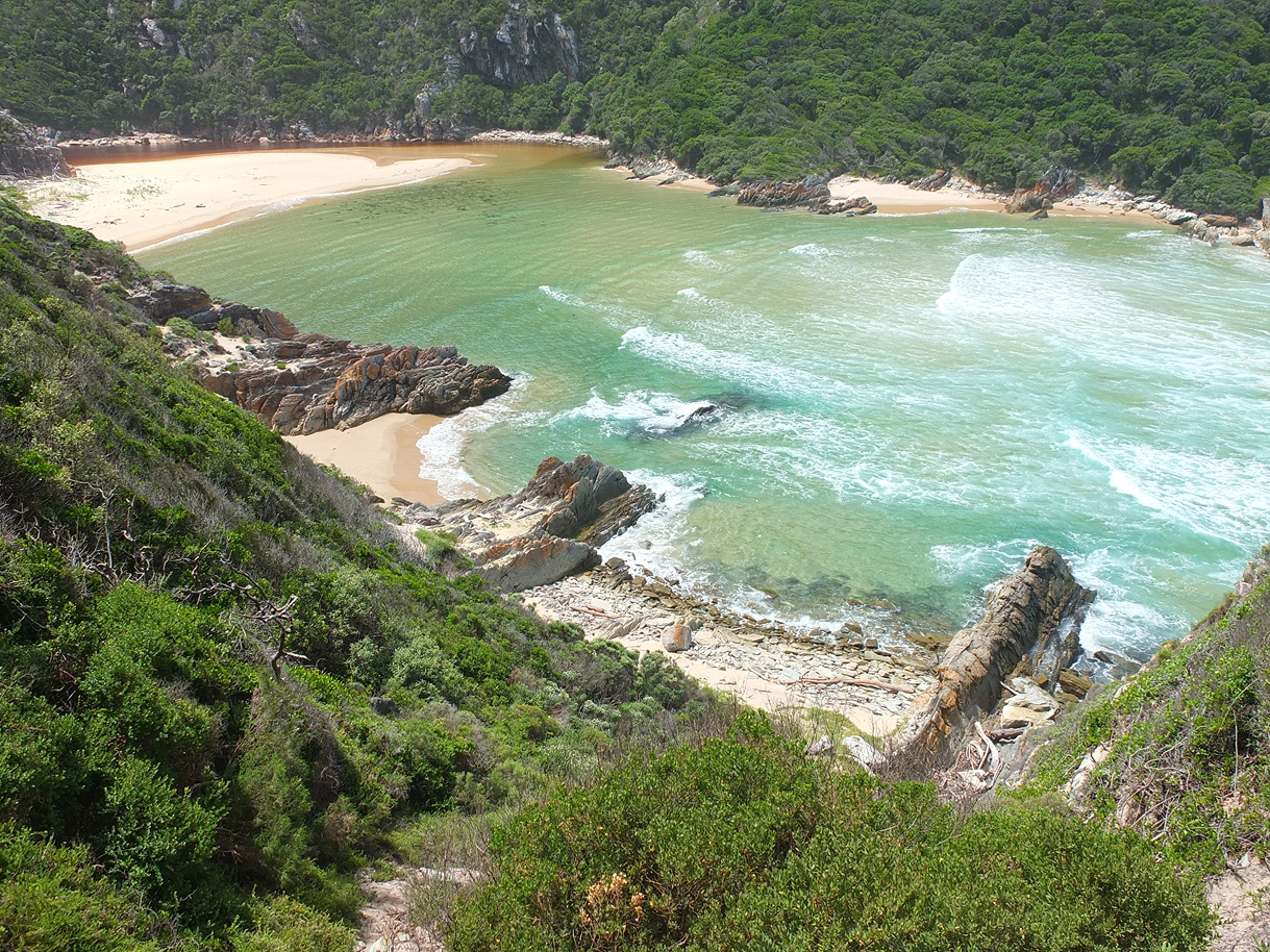 A secluded cove with sandy beach, surrounded by rocky outcrops and lush green vegetation.