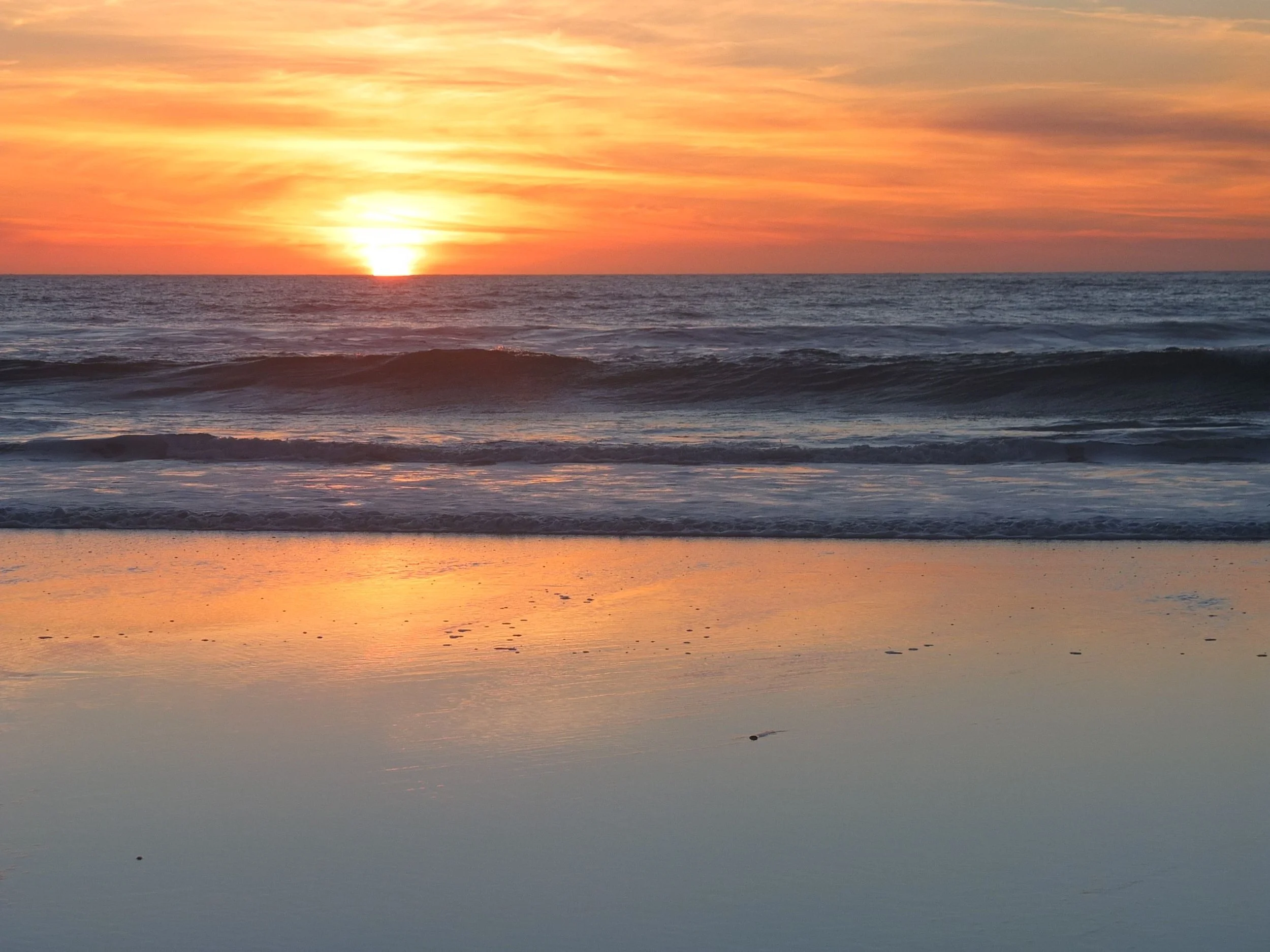 Sunset over the ocean with colorful sky, calm water, and gentle waves