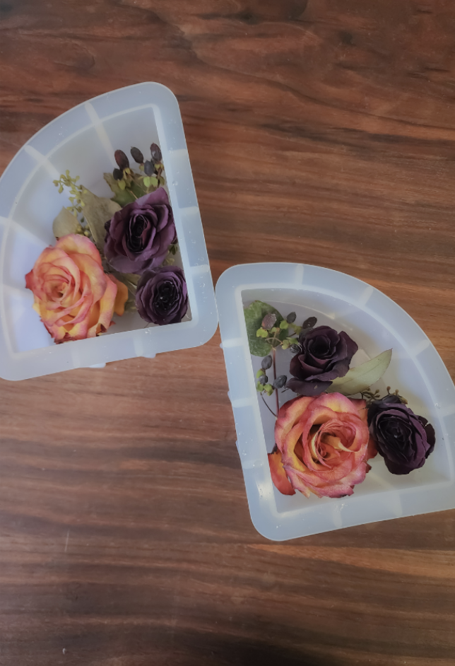 Two small silicone molds filled with assorted dried and preserved flowers, including pink, purple, and yellow roses, placed on a wooden surface.