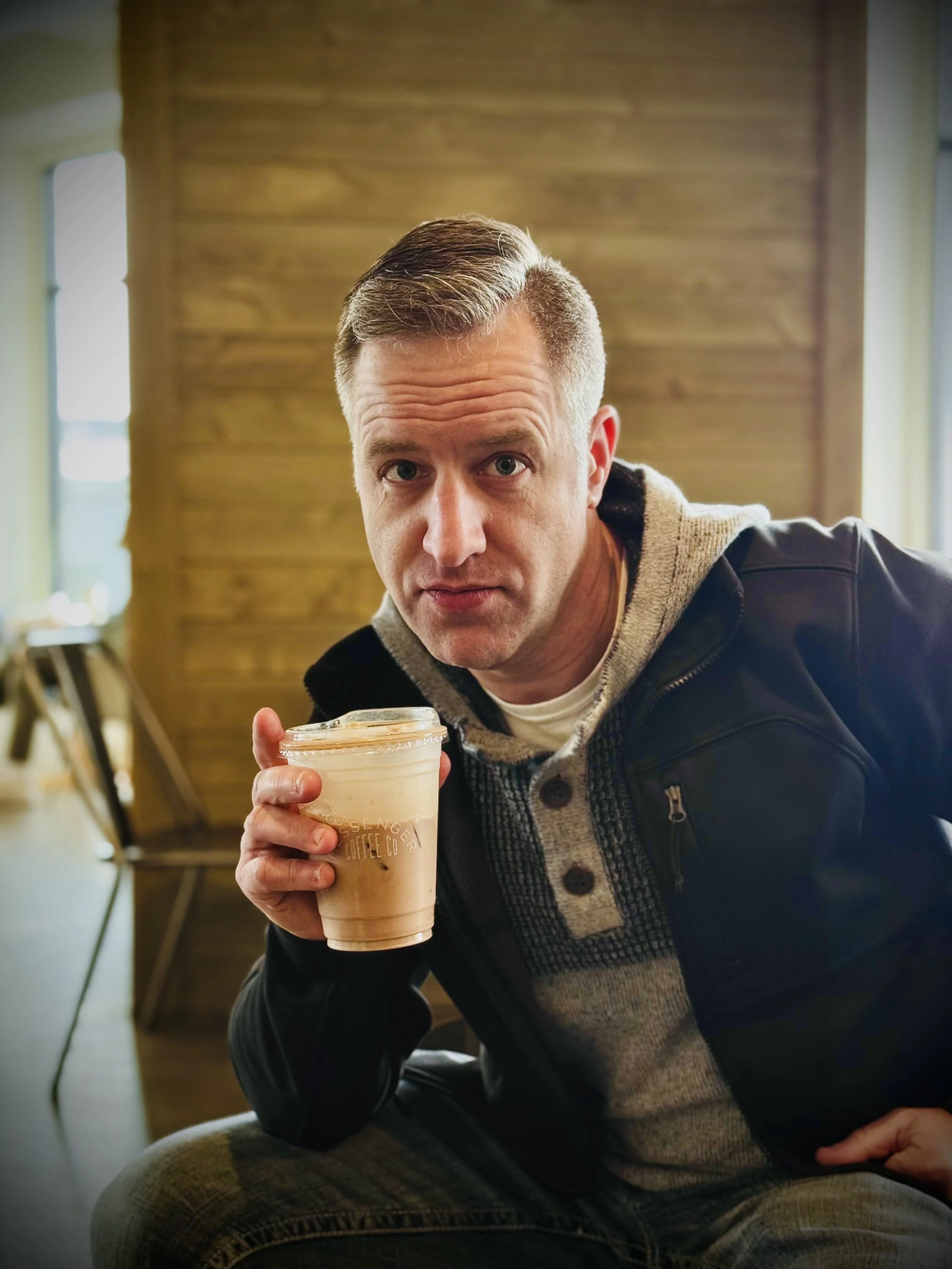 A man holding a glass of iced coffee in a cozy coffee shop with wooden interior decor.