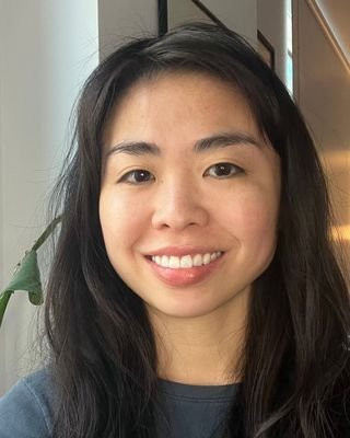 A young woman with long dark hair smiling indoors.
