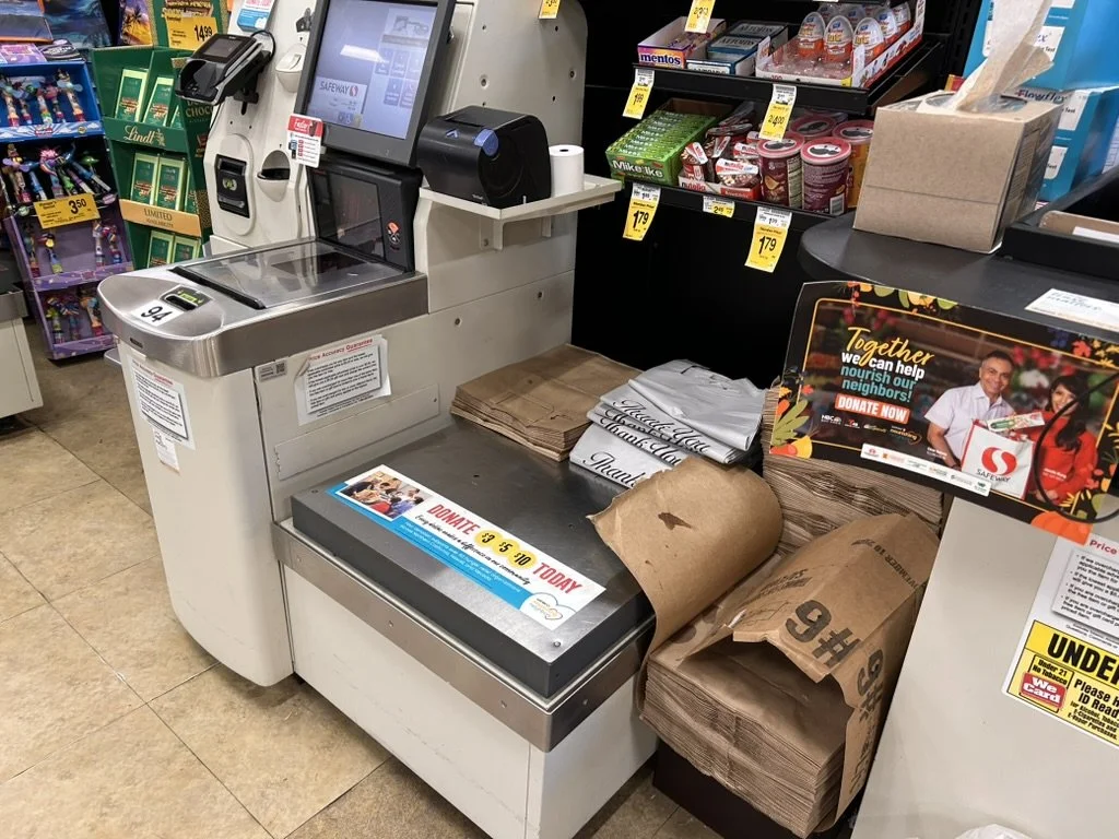 A cash register in a grocery store with both plastic and paper shopping bags