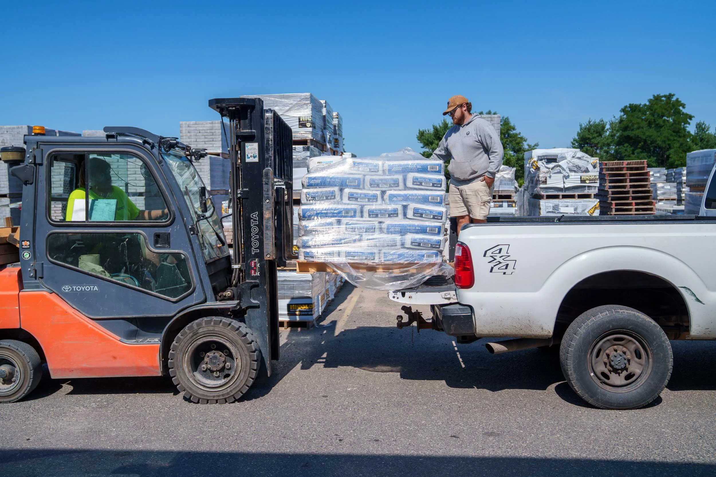 Genest Concrete Biddeford, Maine showroom inventory yard workers using a forklift to load hardscaping materials into a contractor's truck during a commercial photo shoot.