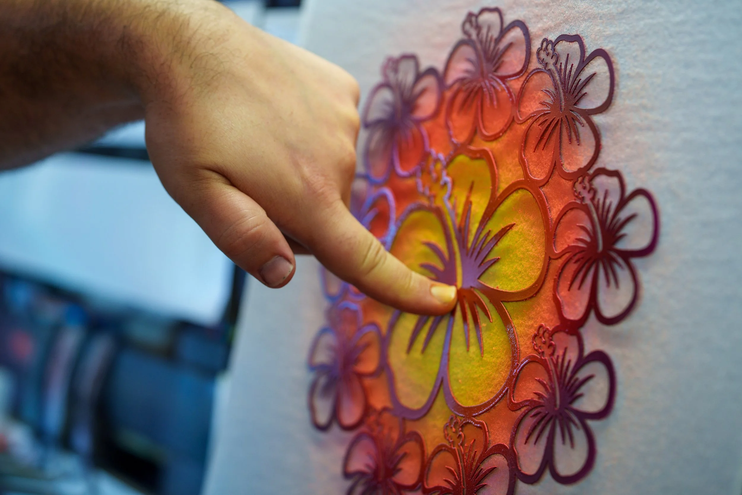 Airbrush painter applying a hibiscus patterned stencil to a custom order airbrushed t-shirt 