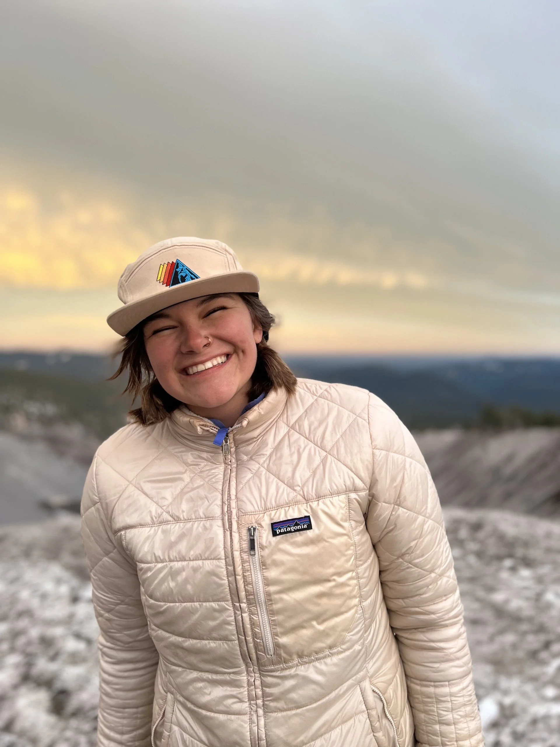 A man with curly dark hair, glasses, and a beard is sitting indoors with a calm expression.