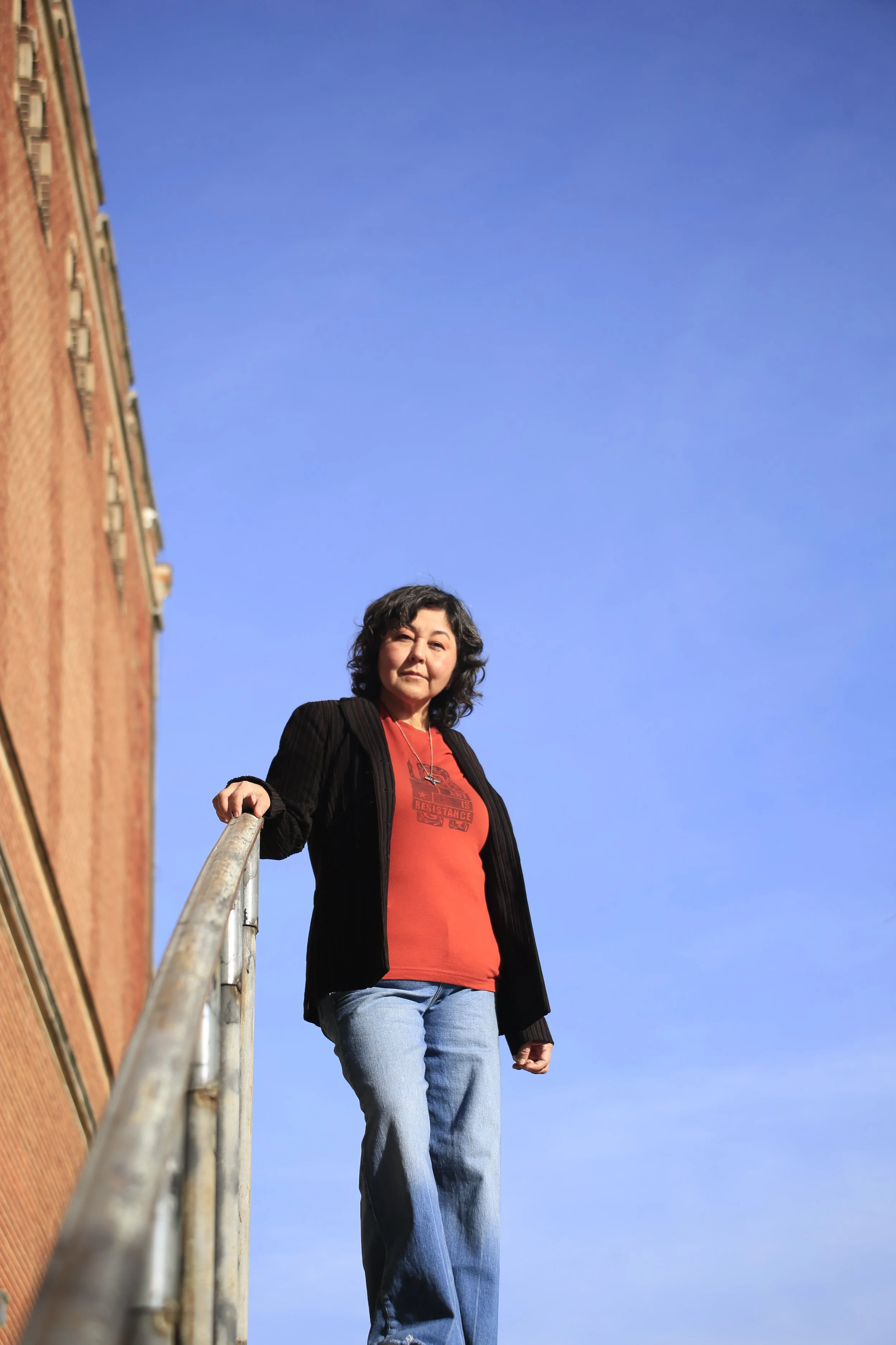A woman standing on an outdoor staircase next to a brick building, with a clear blue sky in the background.