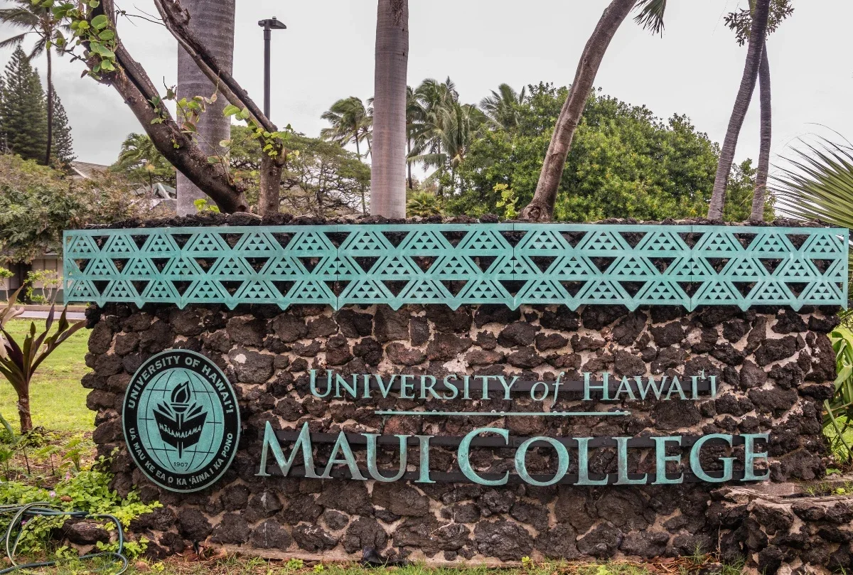Sign for the University of Hawaii Maui College made of dark volcanic rocks with turquoise metal lattice top. Features the university logo and name in turquoise letters.
