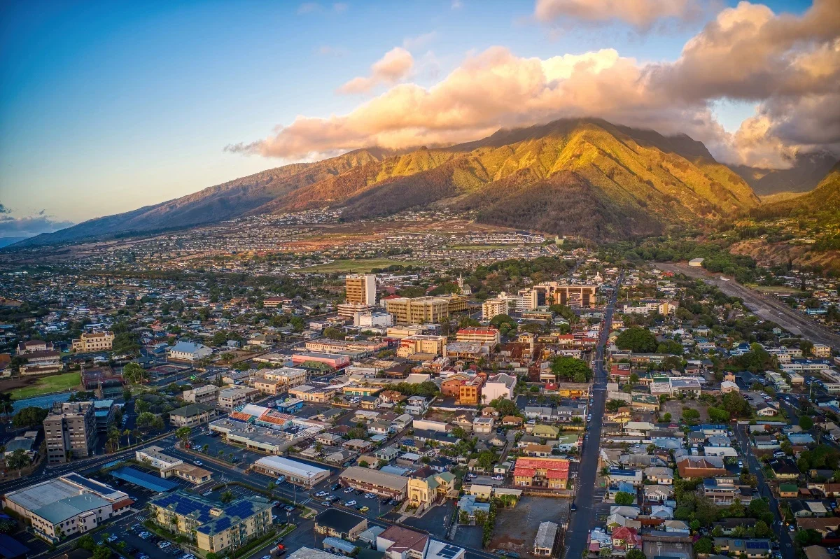 Aerial view of a city with a mountain range in the background, illuminated by sunset light.