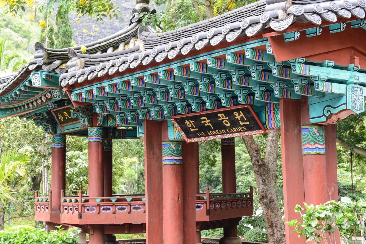 Traditional Korean pavilion with colorful wooden beams and intricate details, surrounded by green trees, labeled 'The Korean Garden'.