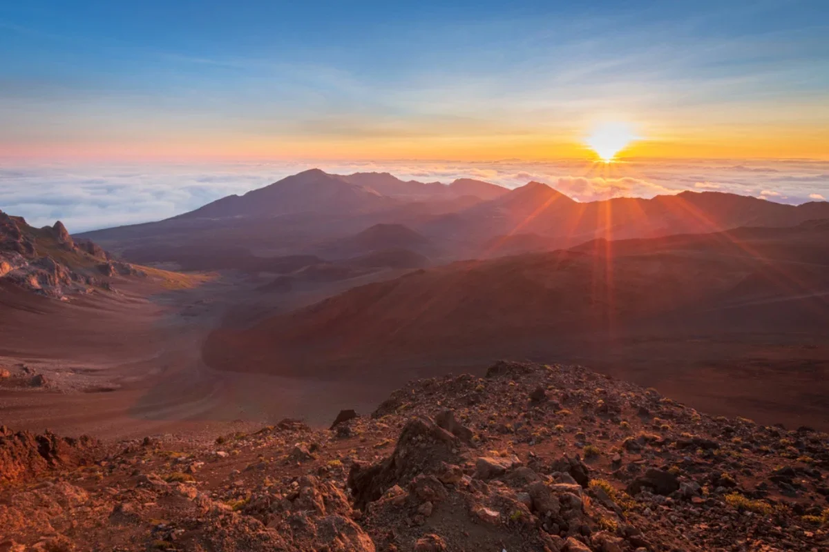 Sunrise over a mountain landscape with rocky terrain and clouds below
