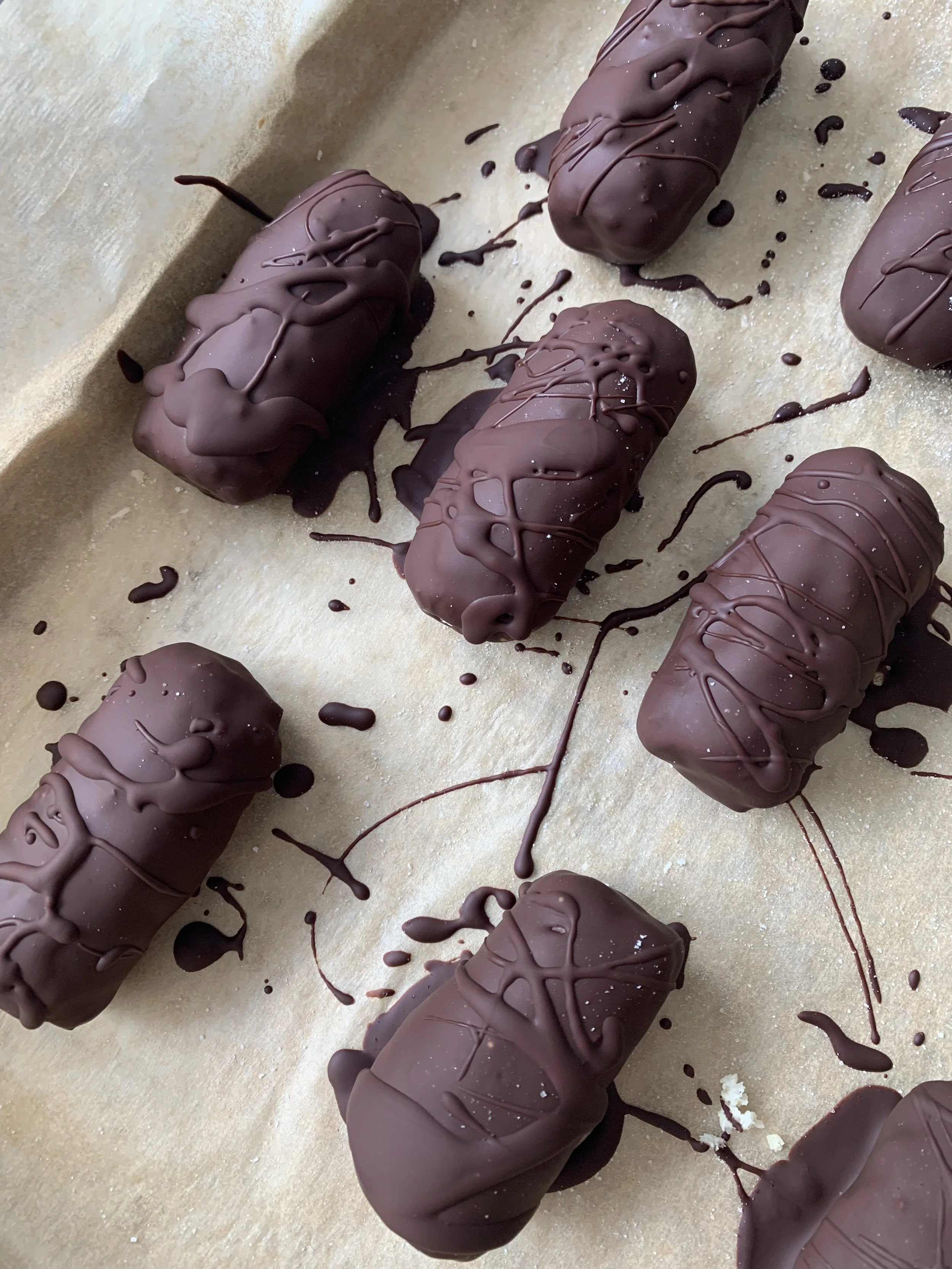 Chocolate-covered eclairs with chocolate drizzle on parchment paper.