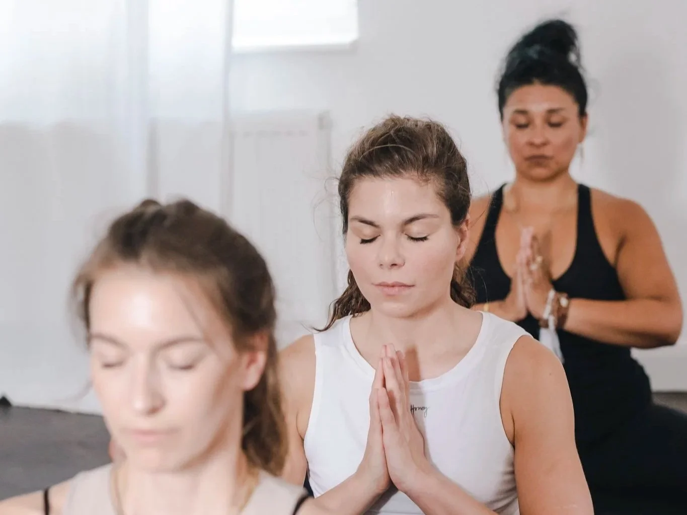 Drei Frauen sitzen im Schneidersitz mit geschlossenen Augen und beten in einem Meditationsraum.