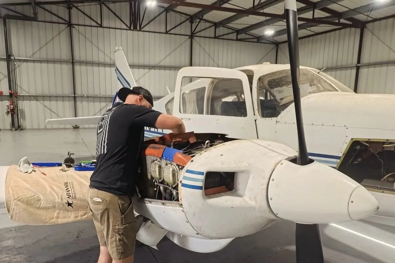 A man working on the engine of a small airplane inside an aircraft hangar.