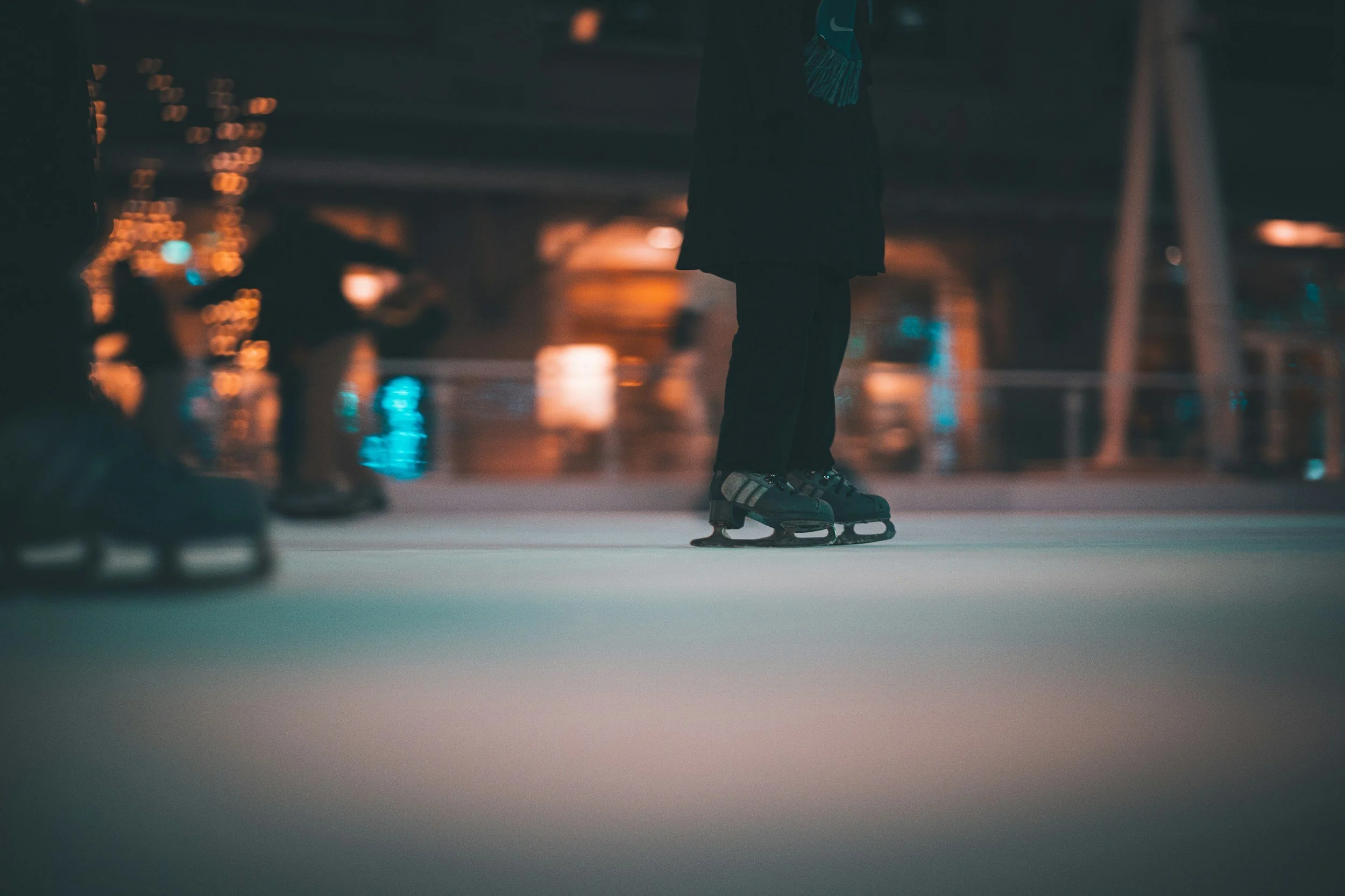 Person ice skating on an indoor rink at night, with blurred colorful lights in the background.