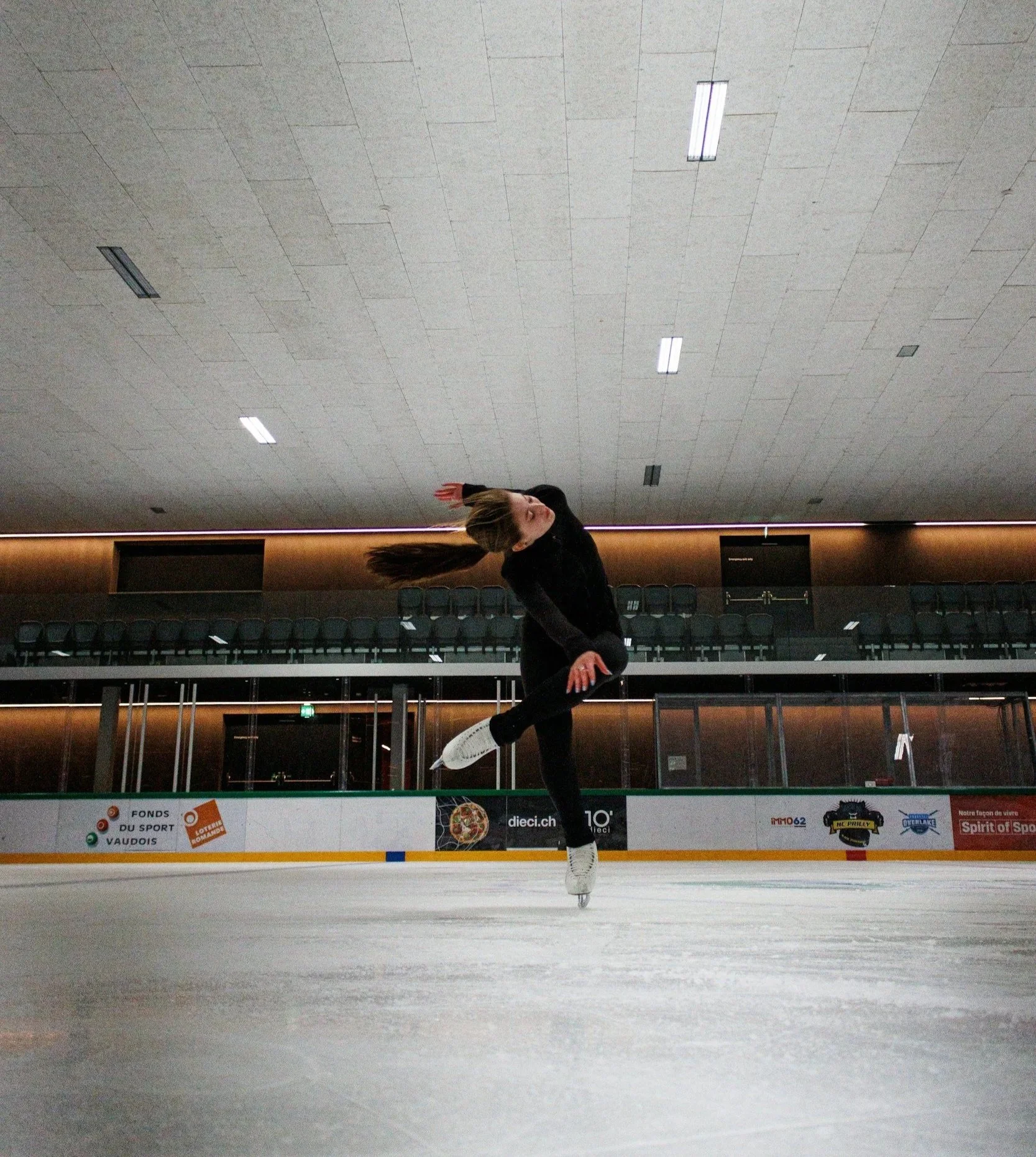 A female figure skater performing a spin on an indoor ice rink.