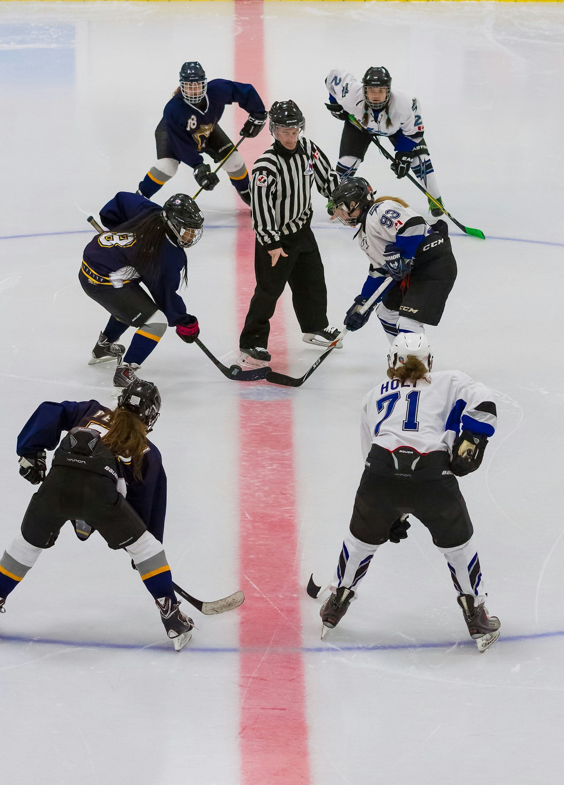 Ice hockey game with players from two teams. Players are in position around the puck with a referee in the middle, on an ice rink.