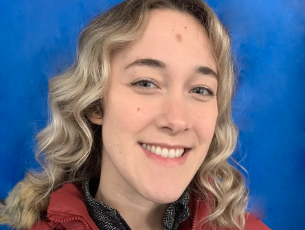 A young woman with wavy blonde hair smiling in front of a blue background.