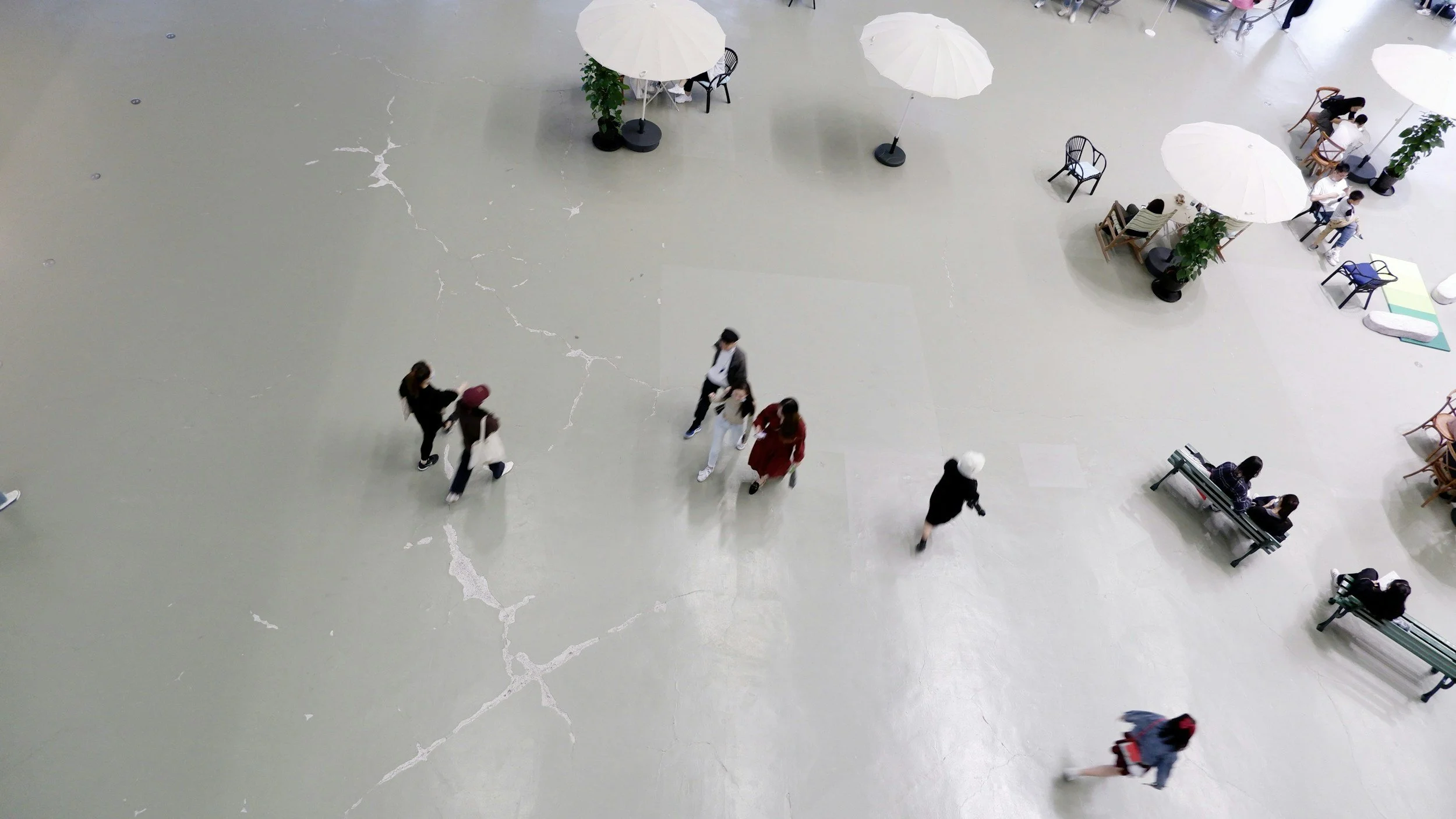 People walking and sitting in a spacious indoor area with a cracked floor and white umbrellas providing shade.