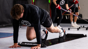 Person in black athletic clothing doing a mountain climber exercise on a mat in a gym.
