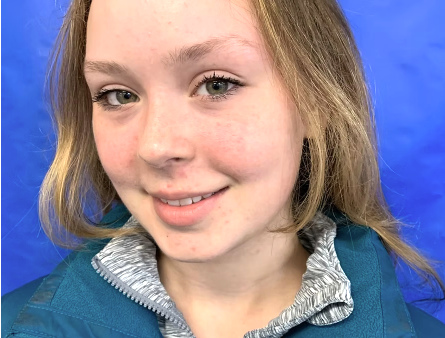 Close-up of a young girl with blonde hair, fair skin, and blue eyes smiling against a blue background.