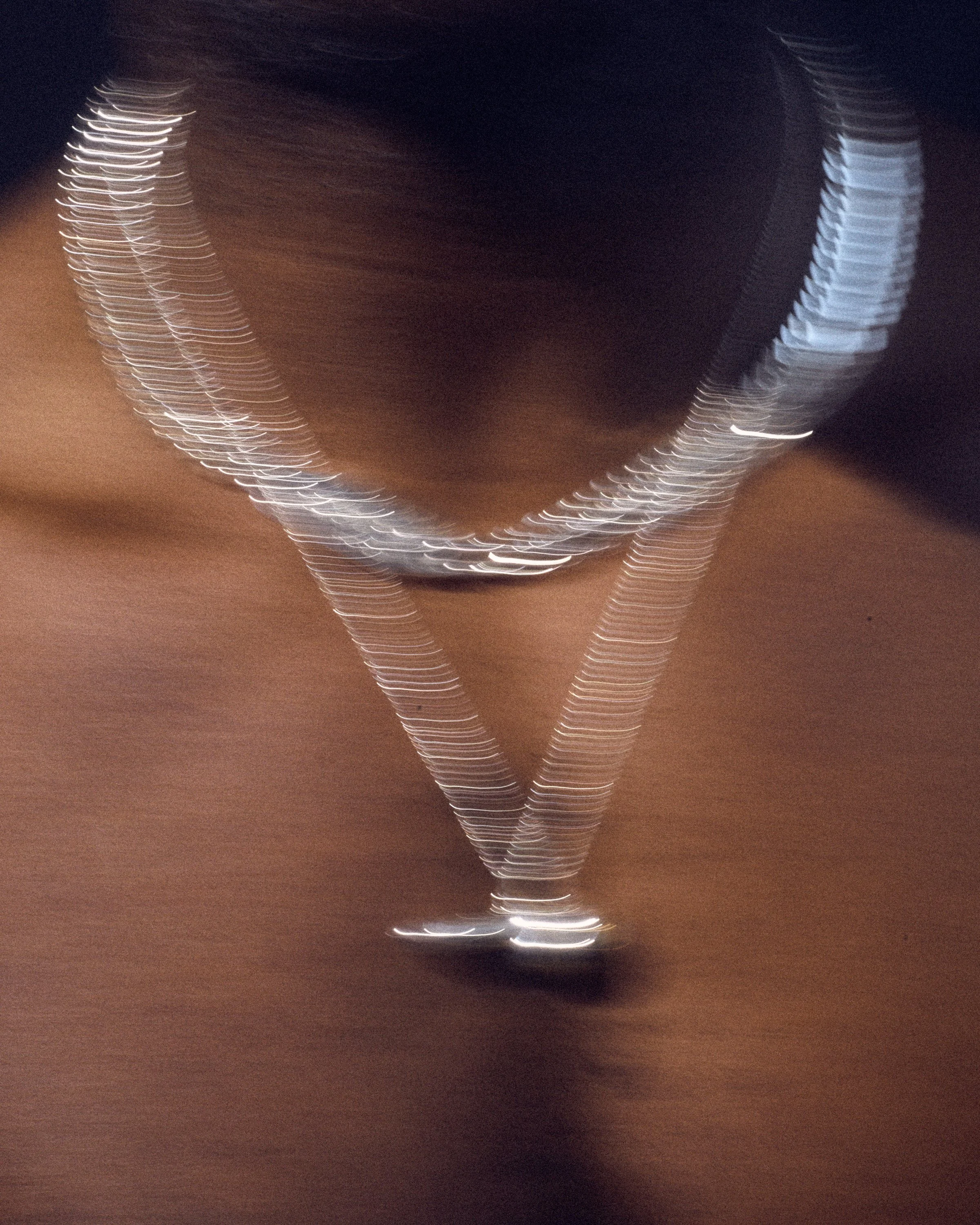 A blurry image of a martini glass with a dark liquid, illuminated by streaks of light, creating a motion effect.