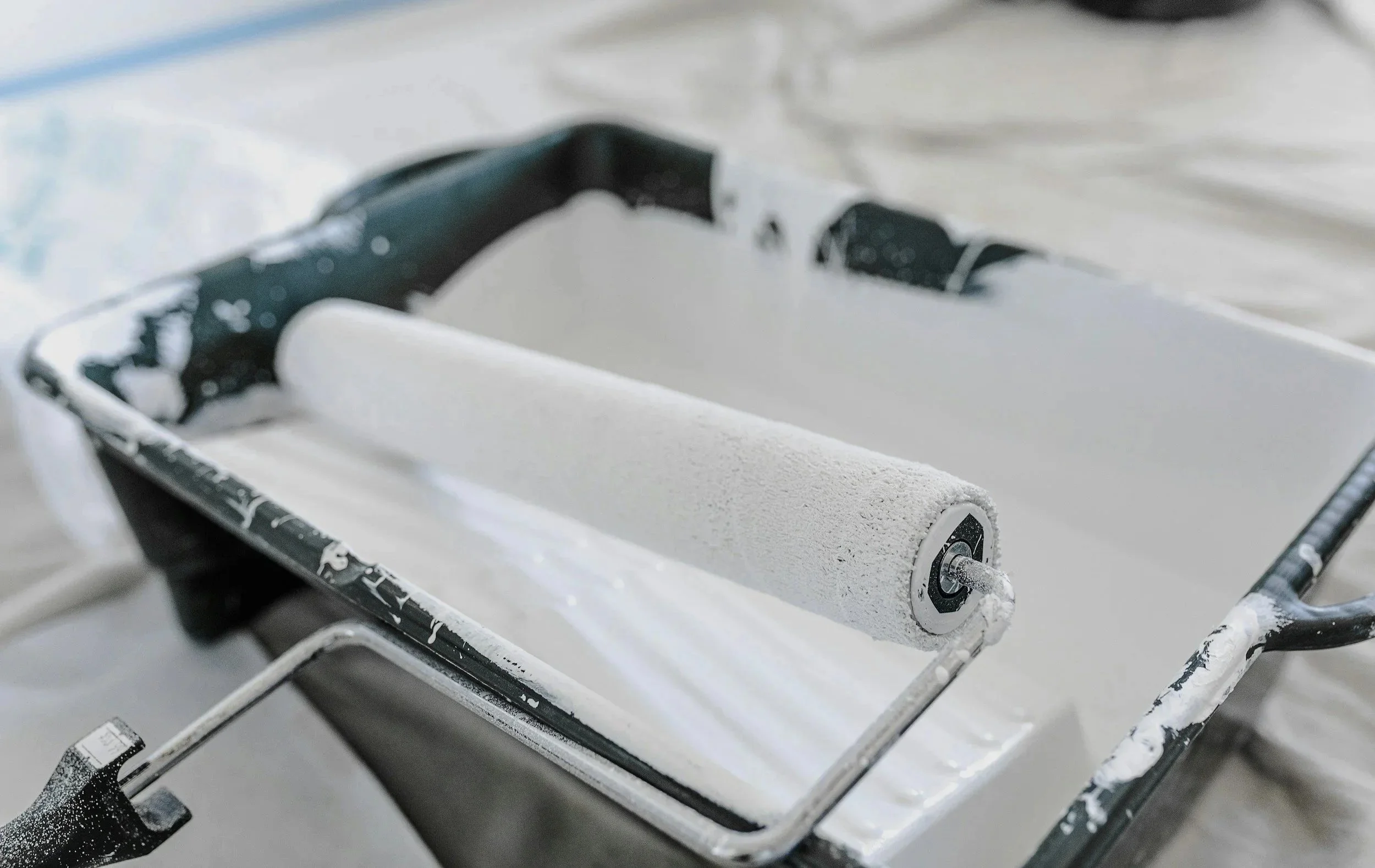 Paint roller covered in white paint resting on a tray with leftover paint.