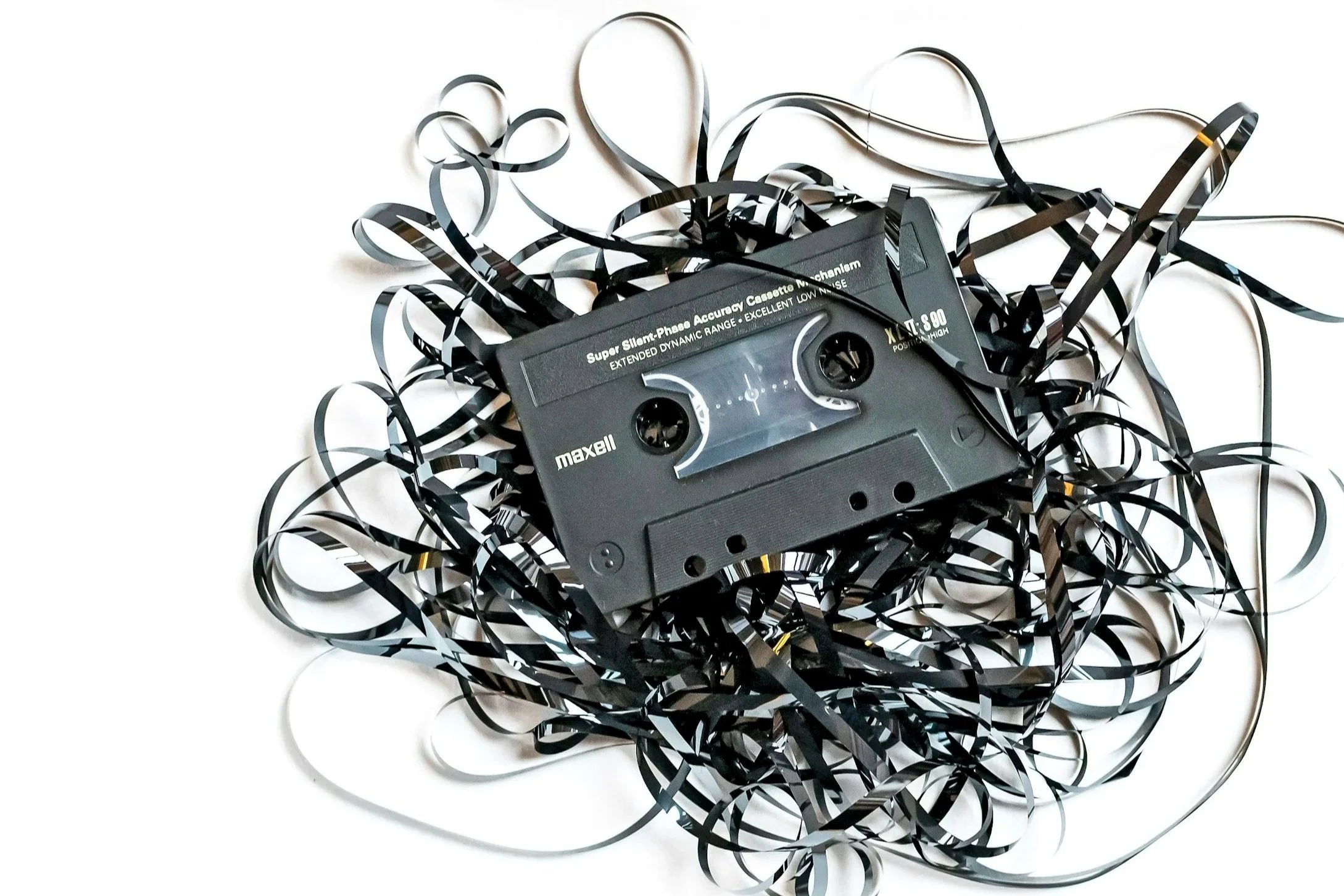 A Maxell cassette tape surrounded by black and white curly tape.