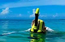 Person snorkeling off the beach in a shallow bay with a clear blue sky overhead.