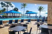 Poolside view with lounge chairs, umbrellas, and palm trees overlooking the ocean at Divi Carina Bay