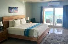 Grapetree Bay Hotel room with a large bed, nightstands, a painting on the wall, and a balcony with a view of the ocean.
