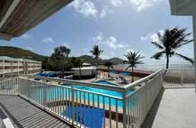 View of a swimming pool area at Divi Carina Bay with lounge chairs, and palm trees under a partly cloudy sky.