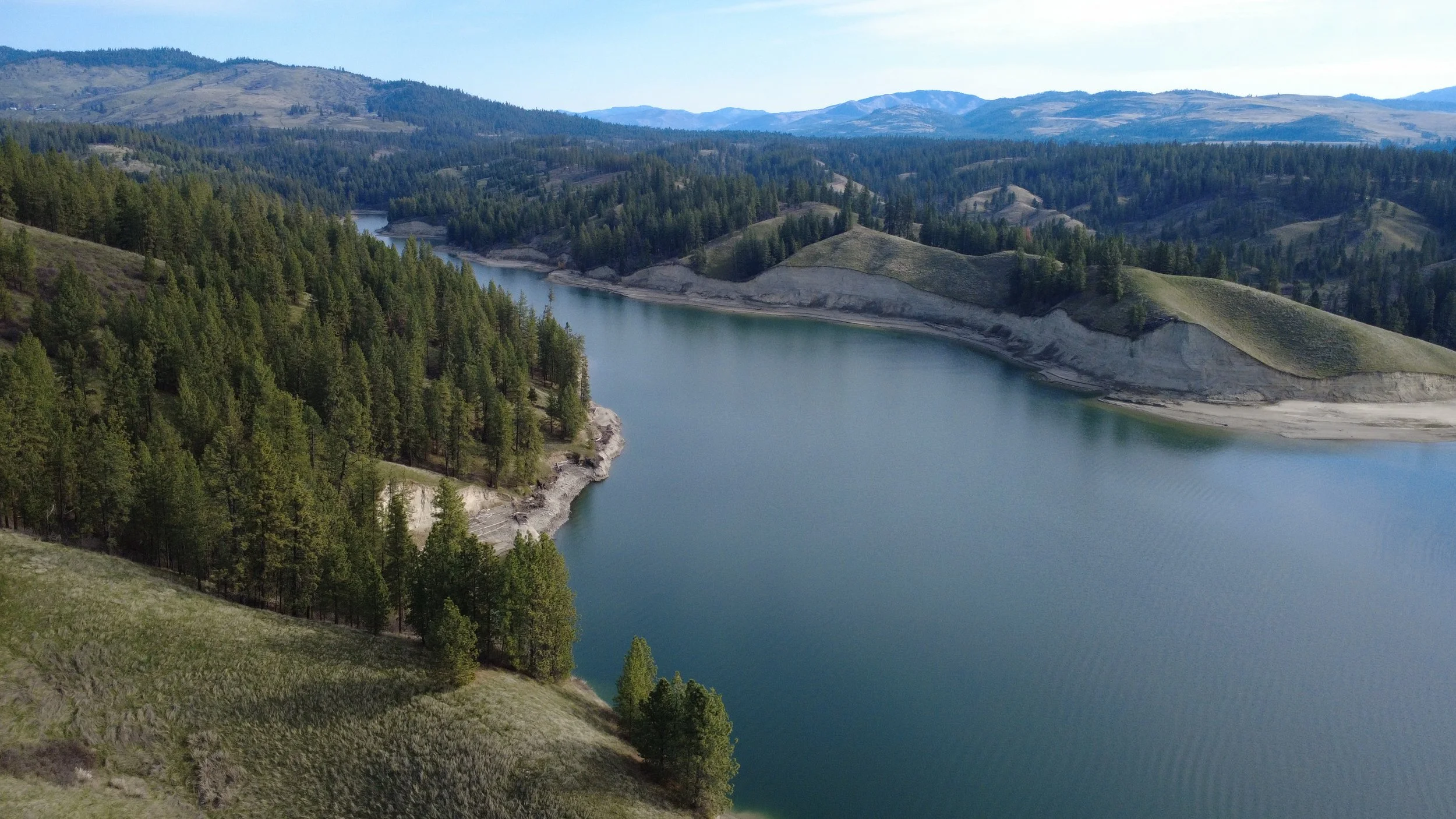 A scenic view of a river flowing through a hilly landscape with green trees and distant mountains under a clear sky.