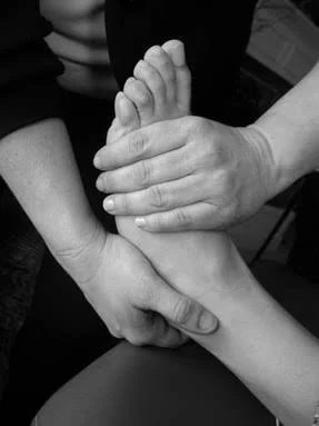A person holding another person's foot while applying light-touch to pressure points along the foot, toes, and ankle.