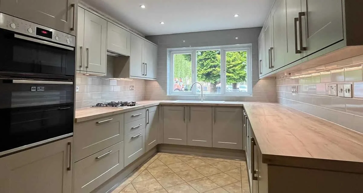 Modern kitchen with light gray cabinets, wooden countertops, a large window with a view of trees, and built-in appliances.