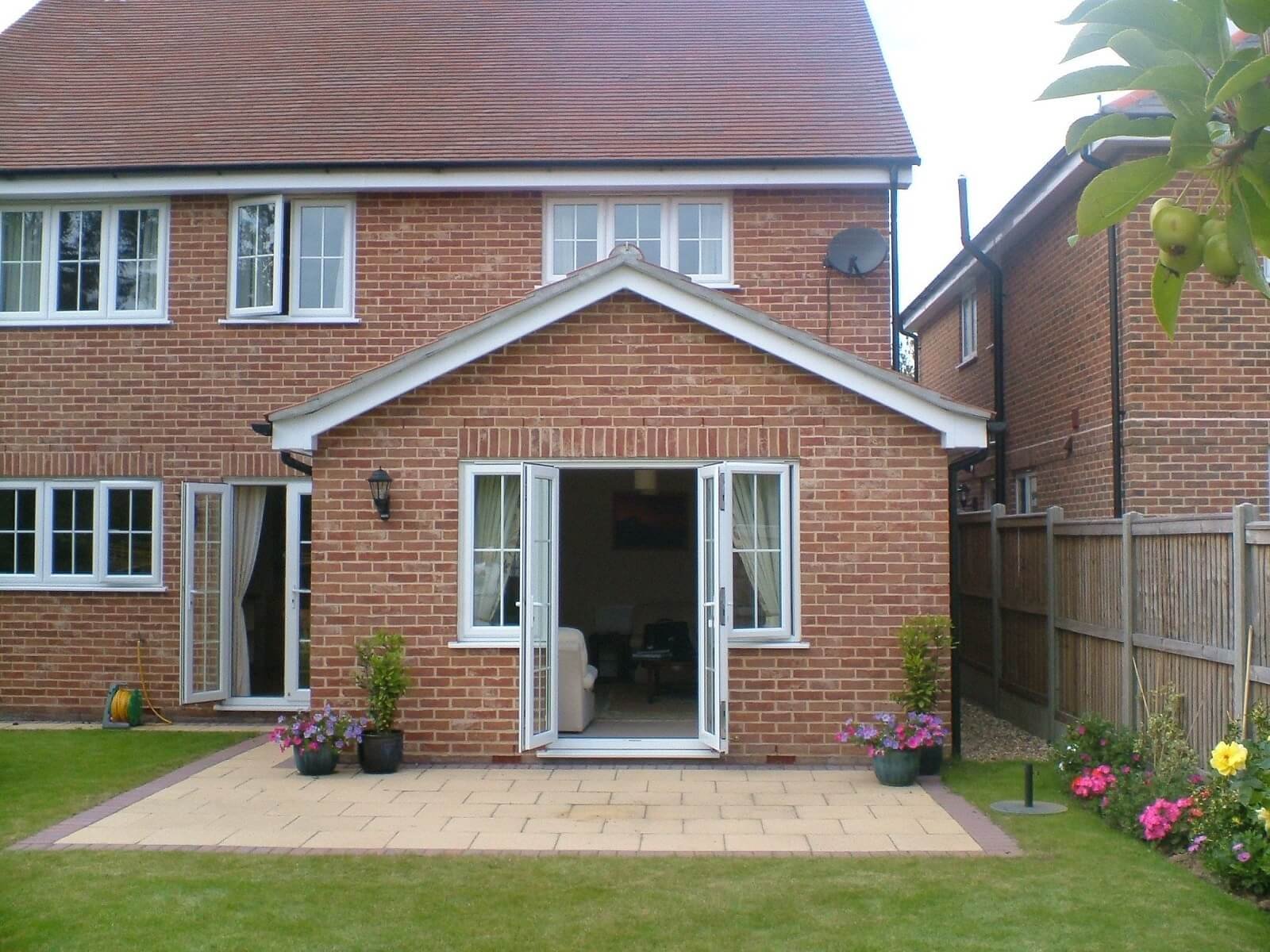Backyard of a brick house with a patio, potted flowers, and open French doors.