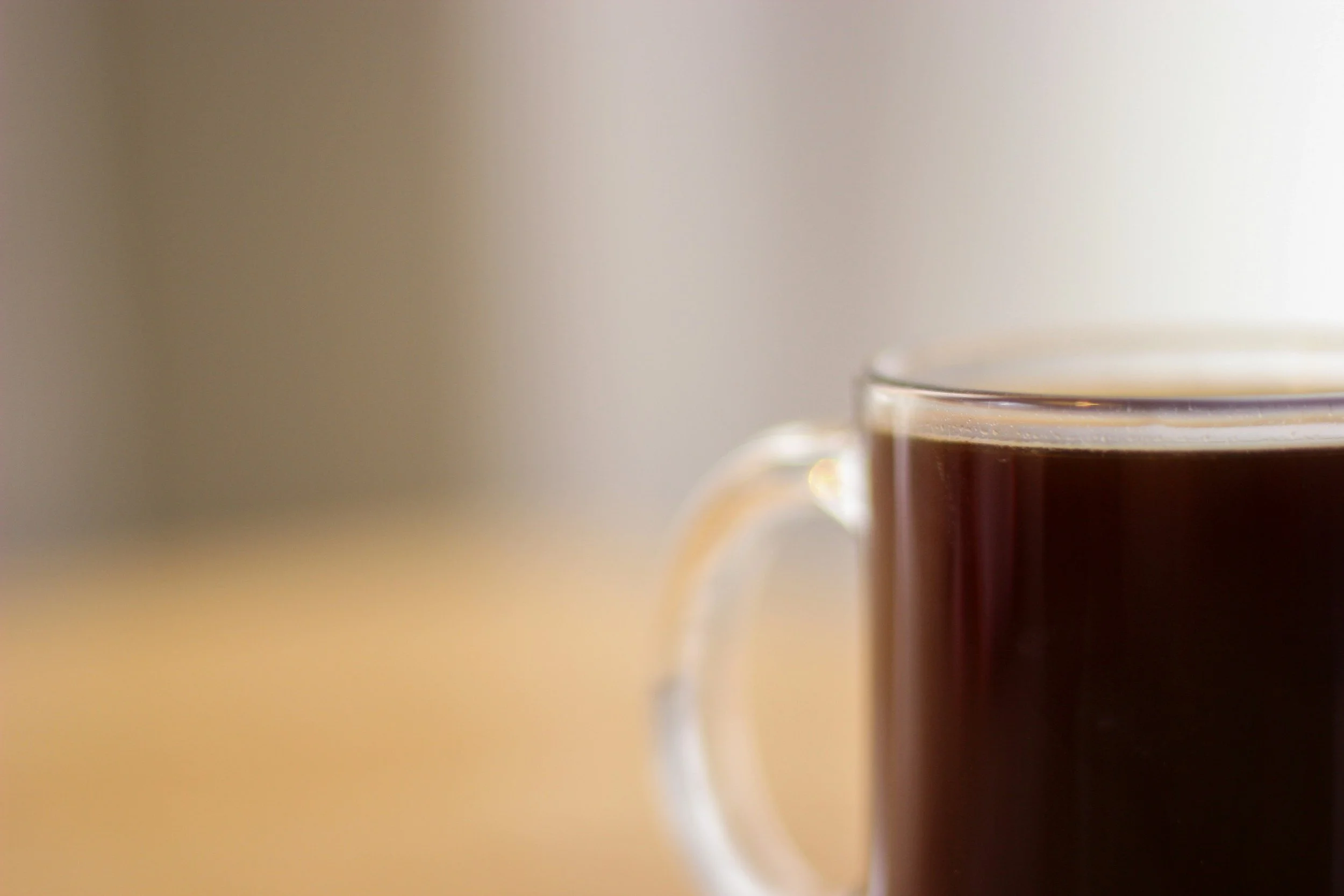 A warm glass mug of coffee resting in soft morning light, creating a quiet, reflective mood on the blog of artist Kim Kelley.